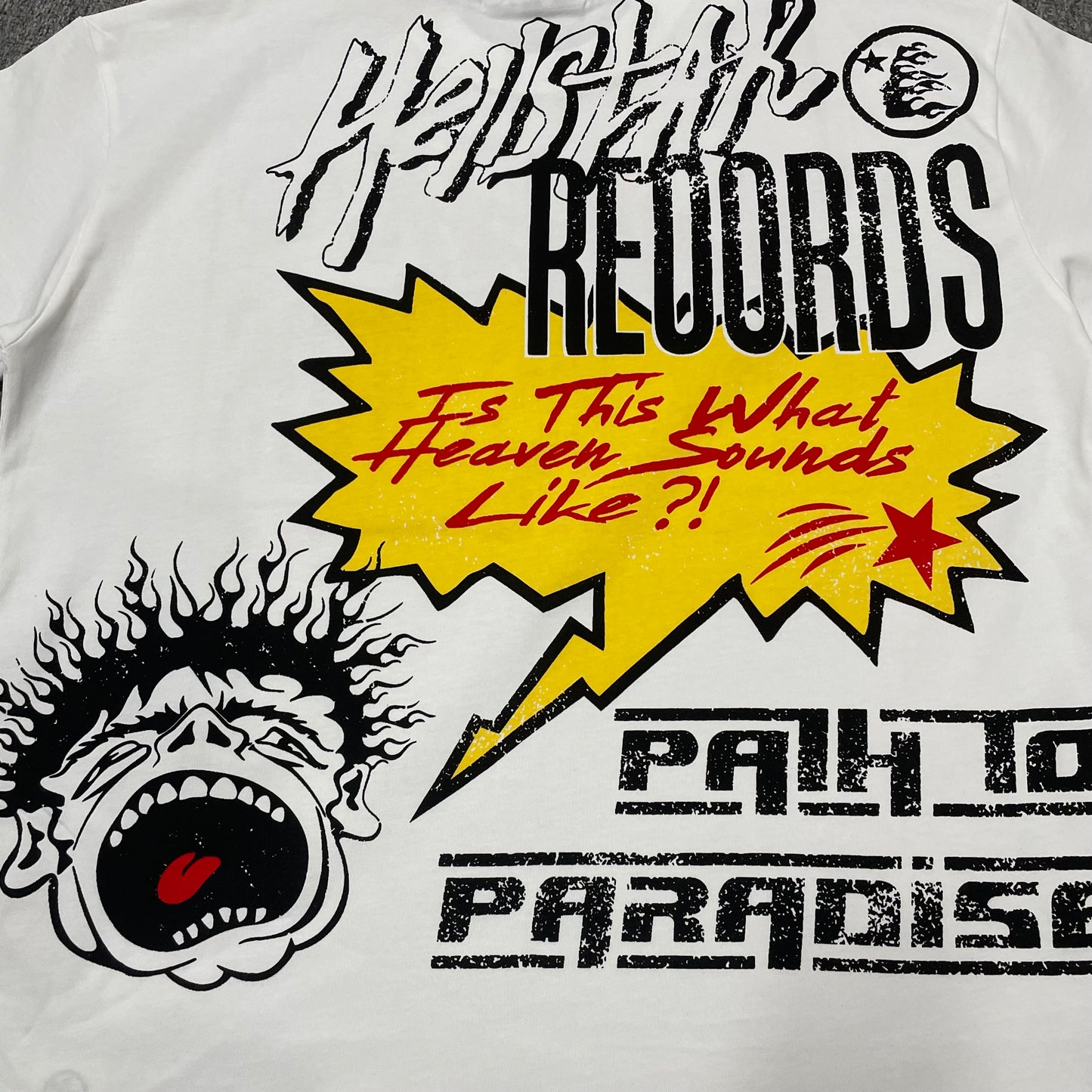Full Hellstar Records Hollywood graphic print on the Path to Paradise T-Shirt
Close-up of the distressed Hellstar Records and Hollywood lettering print
Detailed view of the distressed red black and white print texture on the Hellstar T-Shirt
Oversized screaming-face side graphic with flame details on the Hellstar Path to Paradise T-Shirt
Close-up of the flame and open-mouth side artwork on the Hellstar graphic T-shirt
Full back graphic artwork on the Hellstar Path to Paradise Records T-Shirt