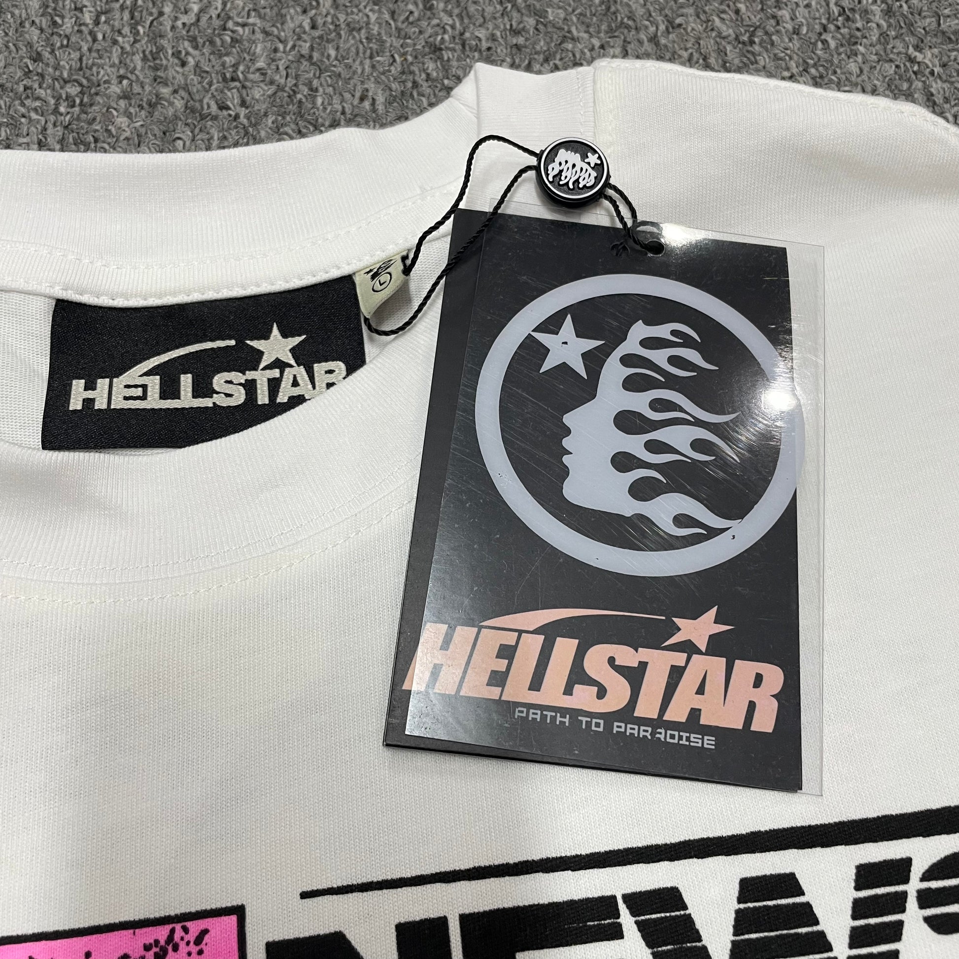 Hellstar branded neck label and crew-neck stitching on the Breaking News T-Shirt
Hellstar Breaking News T-Shirt wash label showing fabric size and garment care information
Size label detail inside the Hellstar Breaking News graphic T-shirt
Hellstar branded hangtag attached to the white Breaking News graphic T-shirt