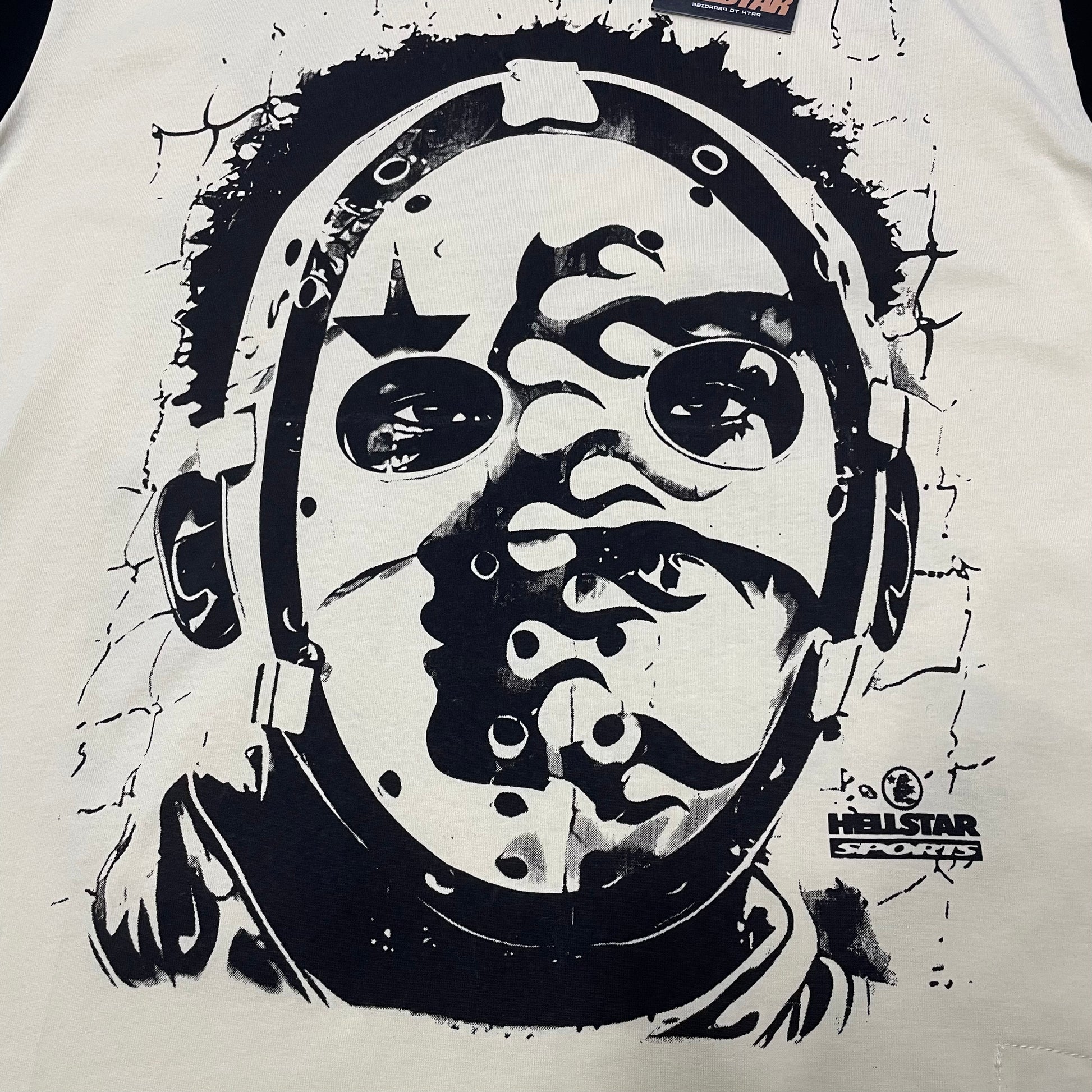 Full oversized helmet face graphic on the front of the Hellstar Helmet Tee
Close-up of the black helmeted face artwork on the Cream Hellstar graphic T-shirt
Detailed view of the distorted face and helmet illustration on the Hellstar Helmet Tee
Hellstar Sports logo detail beside the oversized helmet graphic on the Cream T-shirt