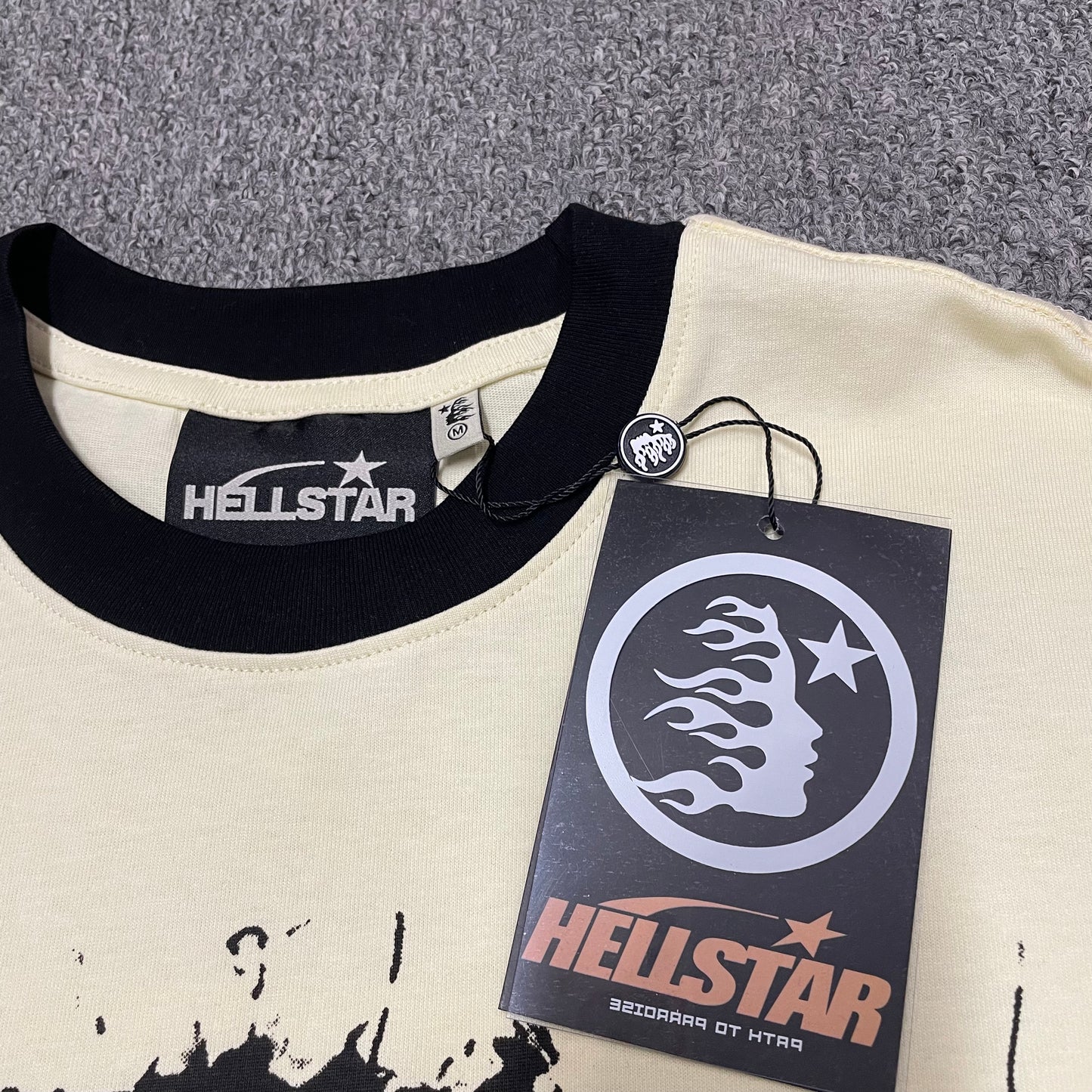 Hellstar branded neck label and contrast crew-neck stitching on the Helmet Tee
Size label detail inside the Cream and Black Hellstar Helmet T-Shirt
Hellstar branded hangtag attached to the Cream Helmet graphic T-shirt