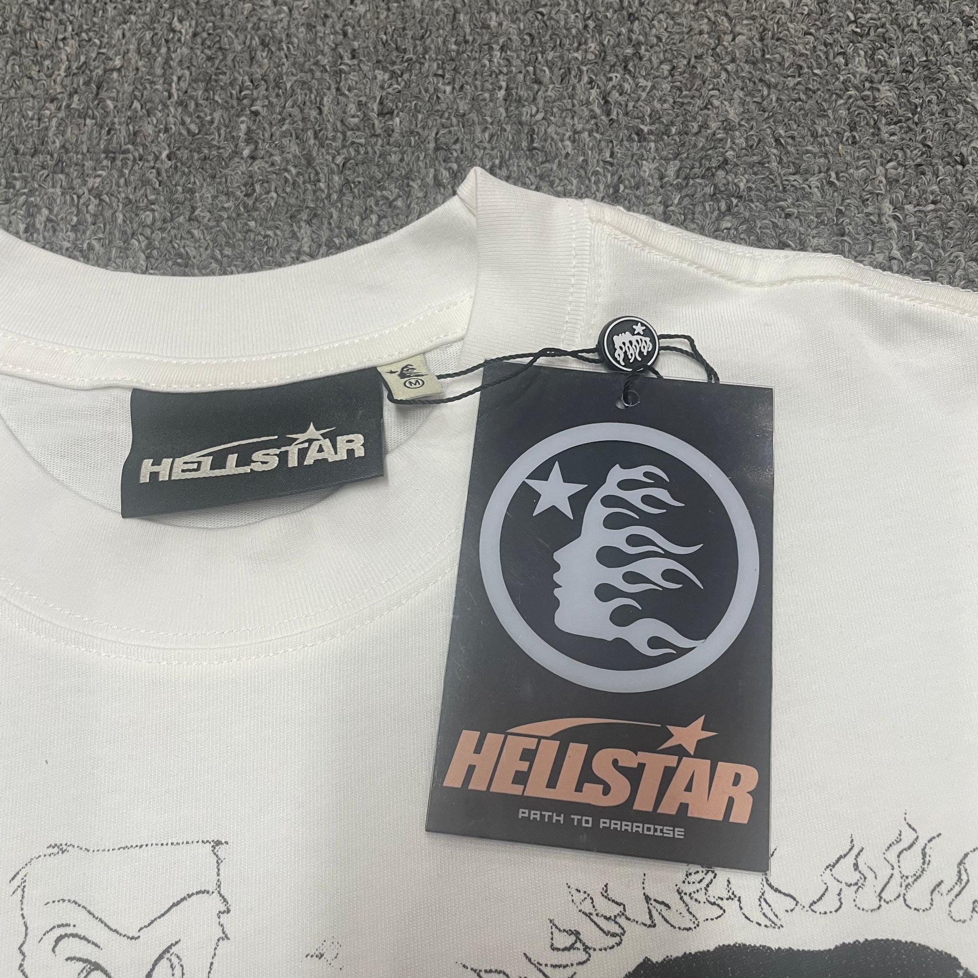 White ribbed crew-neck collar and stitching detail on the Hellstar graphic T-shirt
Size label detail inside the white Hellstar Sports Family graphic T-shirt
Hellstar branded neck label and crew-neck stitching on the Sports Family T-Shirt