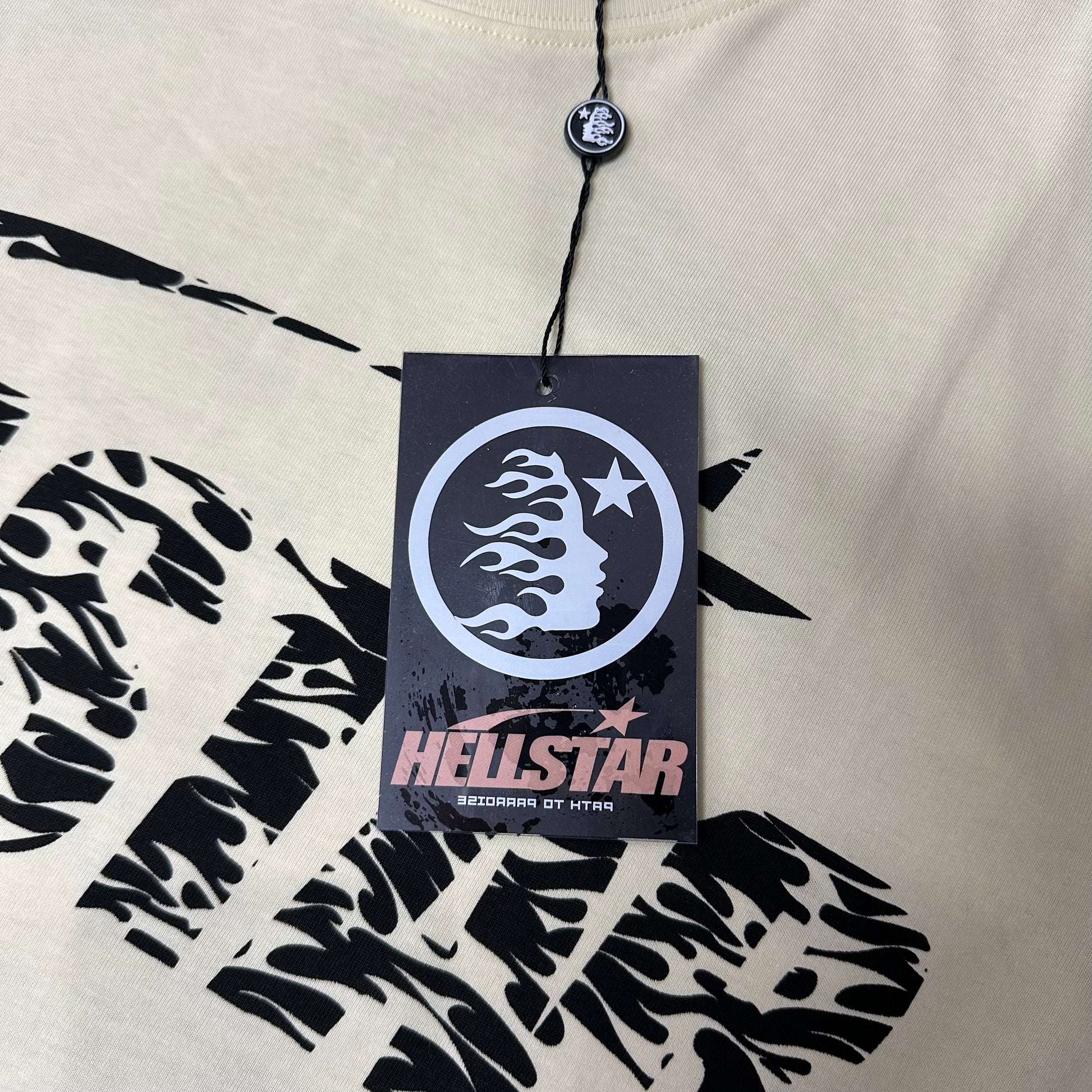 Hellstar branded hangtag attached to the cream Classic Logo graphic T-shirt