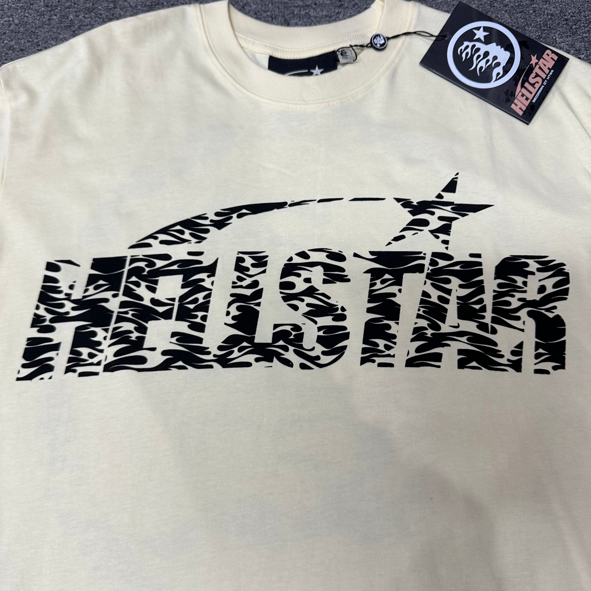 Close-up of the black Hellstar wordmark on the Classic Logo cream T-shirt
Bold Hellstar logo lettering printed across the front of the cream graphic T-shirt
Flame-pattern artwork inside the black Hellstar logo lettering
Black shooting-star graphic above the Hellstar Classic Logo lettering