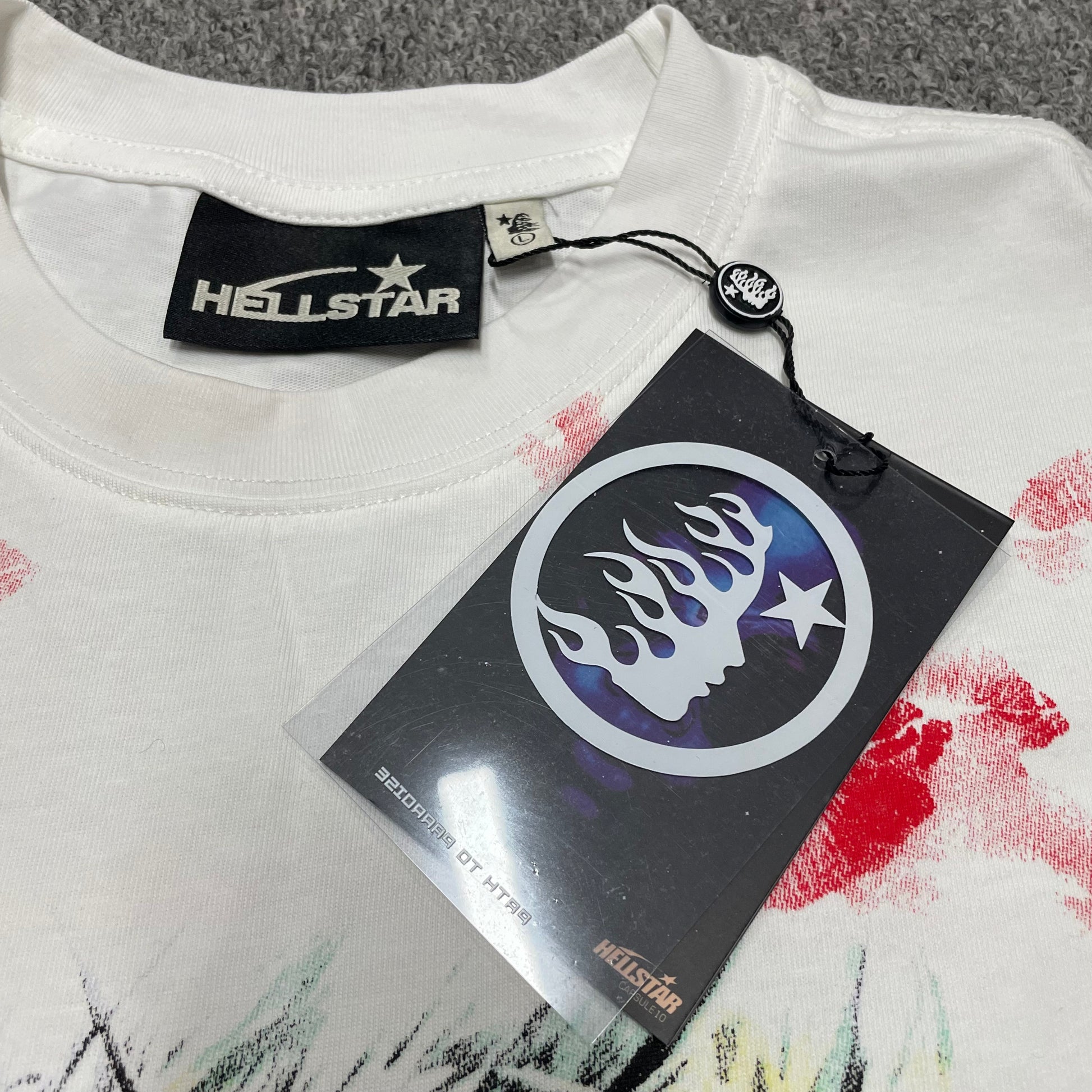 Hellstar branded neck label and crew-neck stitching on the French Kiss T-Shirt
White ribbed crew-neck collar and stitching detail on the Hellstar French Kiss T-Shirt
Size label detail inside the white Hellstar French Kiss graphic T-shirt
Front view of the Hellstar flame and star logo hangtag