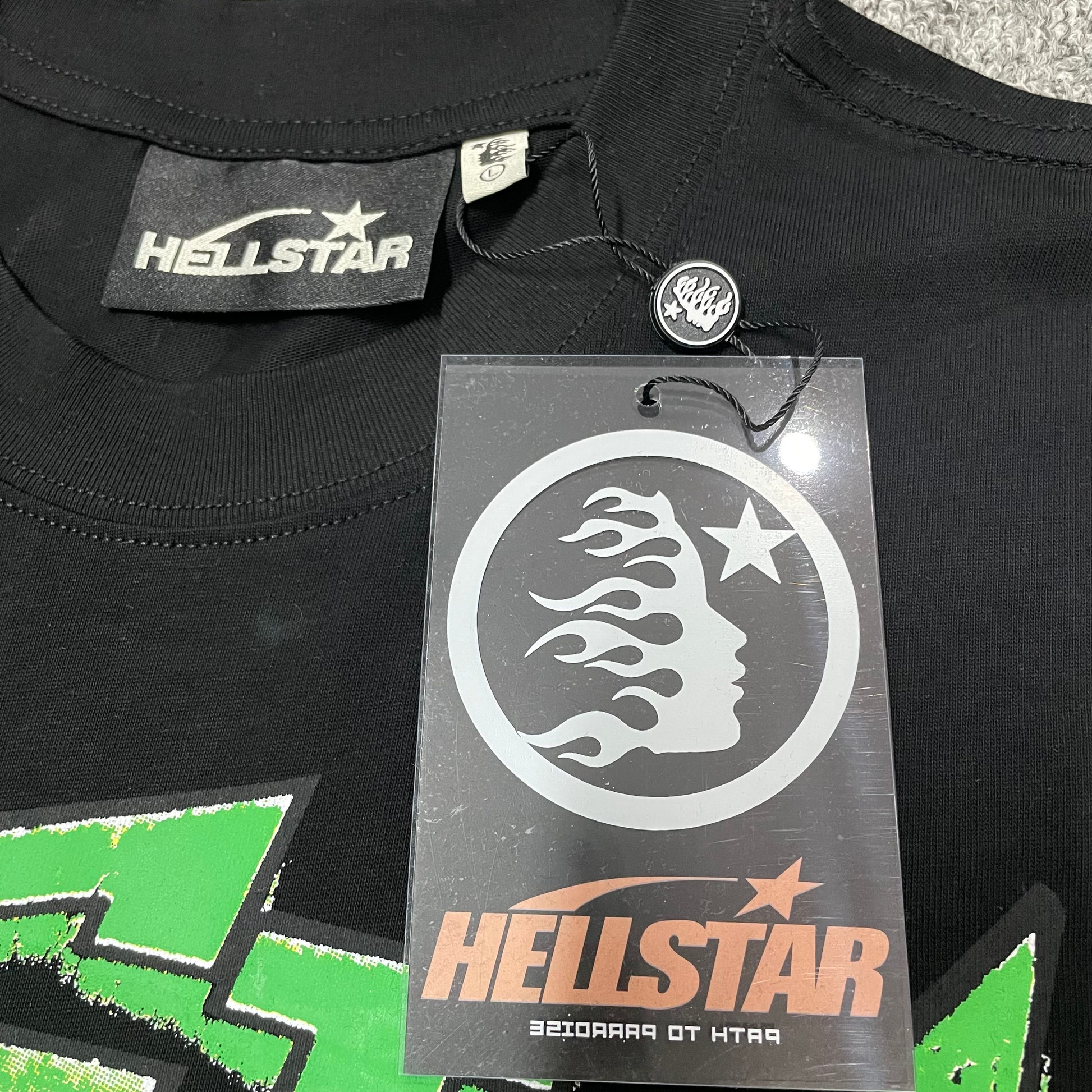 Hellstar branded neck label and crew-neck stitching on The Future T-Shirt
Black ribbed crew-neck collar and stitching detail on the Hellstar graphic T-shirt
Size label detail inside the black Hellstar The Future graphic T-shirt
Front view of the Hellstar flame and star logo hangtag