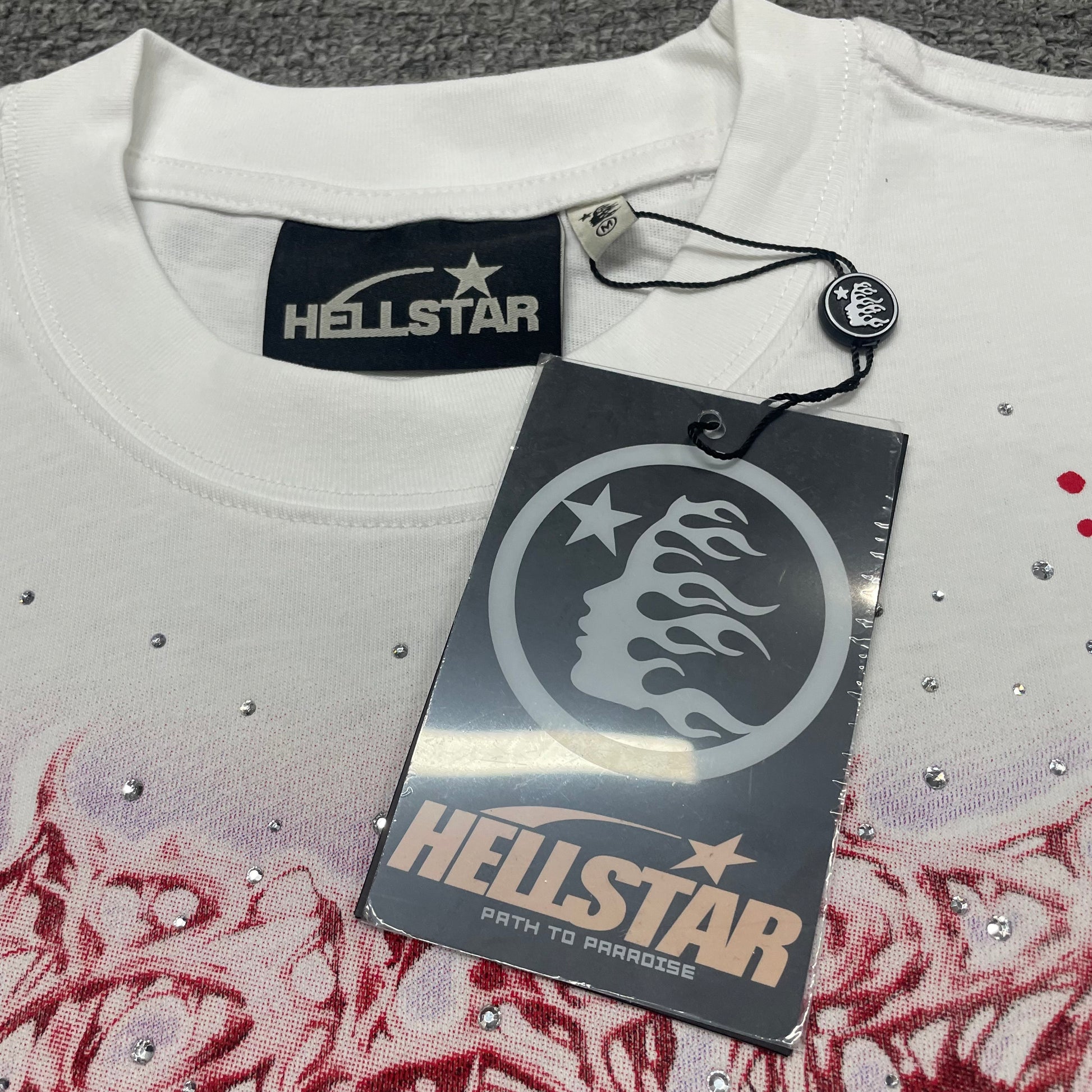 Hellstar woven neck label inside Red Face white graphic T-shirt
Hellstar size label detail on Red Face white graphic T-shirt
Hellstar branded hangtag attached to Red Face rhinestone graphic T-shirt
