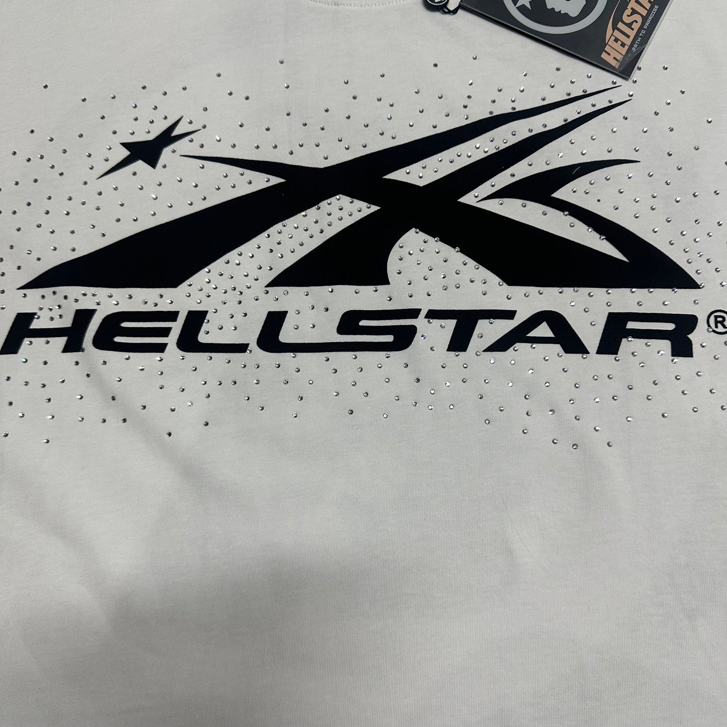 Full black Hellstar classic logo graphic on white rhinestone T-shirt
Full rhinestone decoration surrounding the Hellstar logo on white T-shirt
Detailed crystal placement around the Hellstar logo graphic
Black Hellstar classic logo graphic detail on white T-shirt