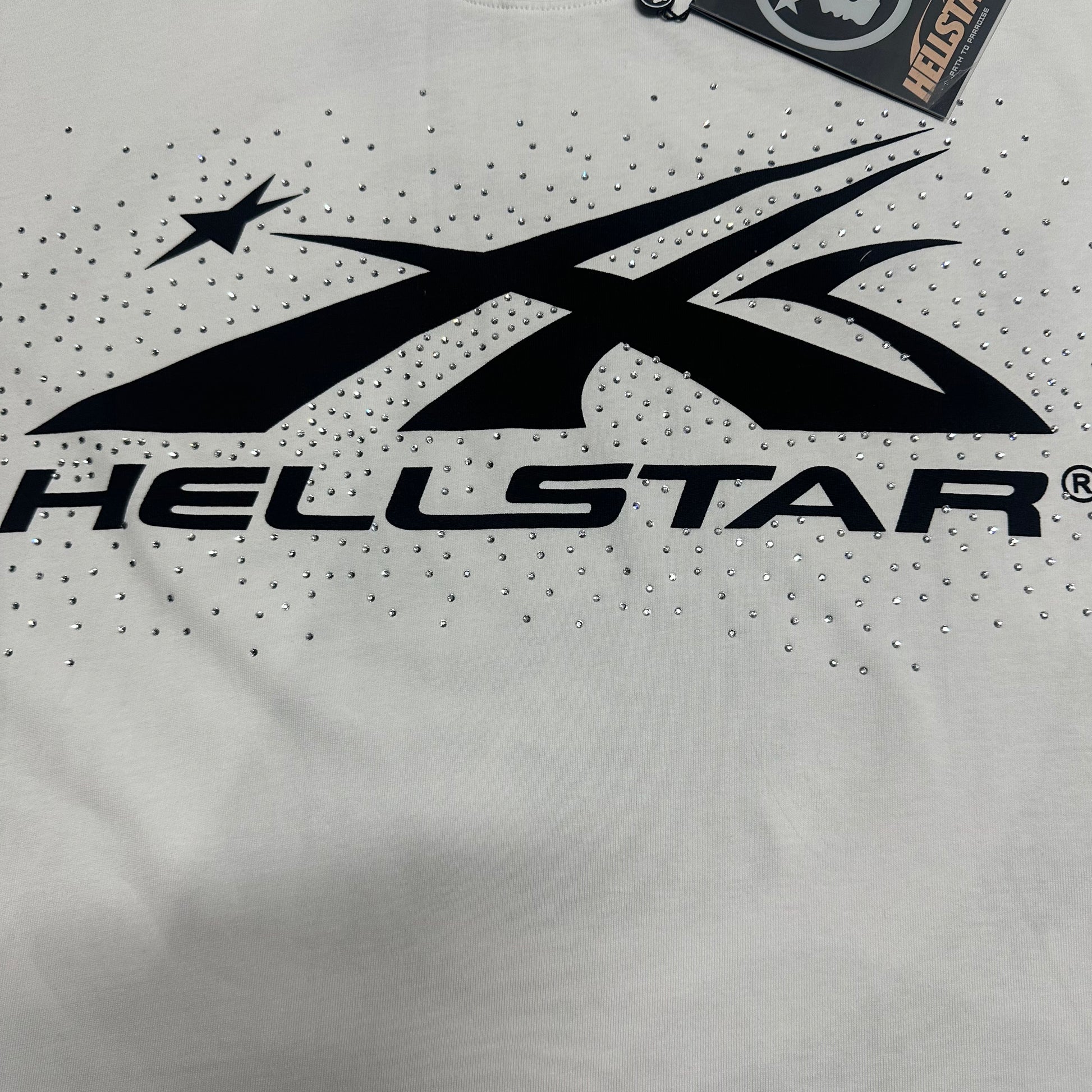 Full black Hellstar classic logo graphic on white rhinestone T-shirt
Full rhinestone decoration surrounding the Hellstar logo on white T-shirt
Detailed crystal placement around the Hellstar logo graphic
Black Hellstar classic logo graphic detail on white T-shirt