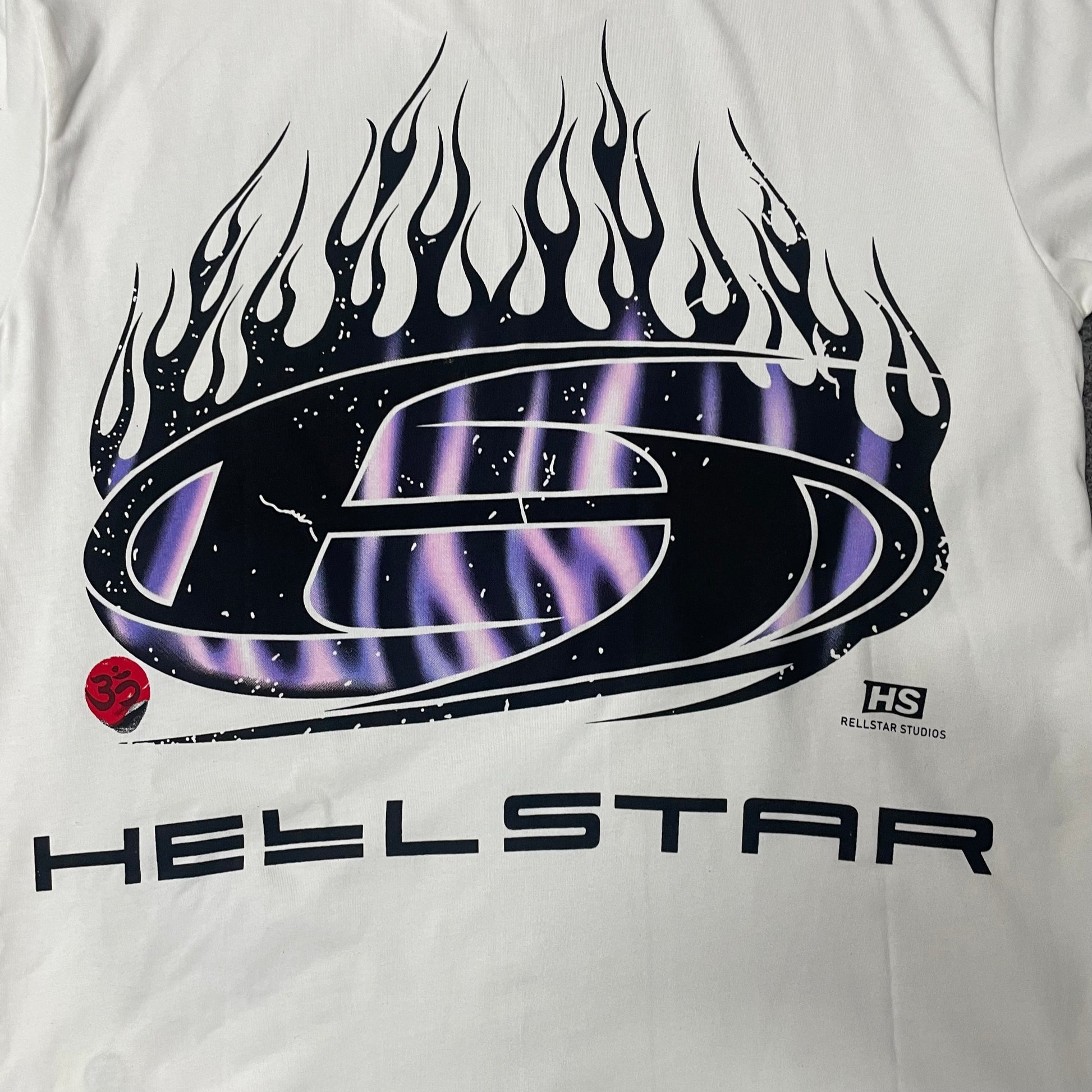 Full oval H logo and blue-purple flame graphic on Hellstar white T-shirt
Close-up of the oval H logo and blue flame print on Hellstar white T-shirt
Detailed black outlines and blue-purple flame artwork on Hellstar H Blue Flame Tee
Blue and purple flame print detail on Hellstar H Blue Flame white T-shirt
Oval H logo graphic detail on Hellstar H Blue Flame T-shirt
Red Om symbol graphic detail on Hellstar H Blue Flame white T-shirt