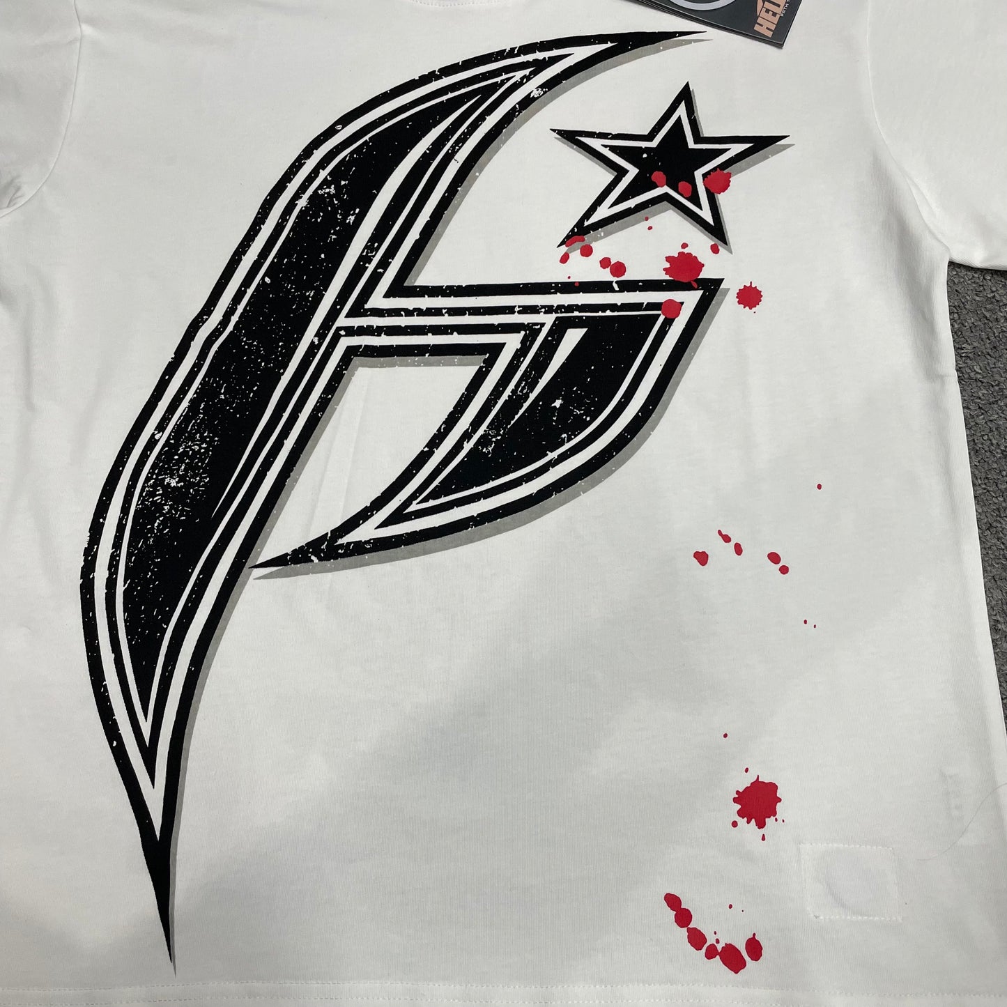Full oversized black H Star graphic on Hellstar white T-shirt
Close-up of the oversized H Star print on Hellstar white T-shirt
Detailed black distressed graphic and red splatter print on Hellstar H Star Tee
Close-up of the screen-print texture on Hellstar H Star graphic T-shirt
Large black H logo graphic detail on Hellstar white T-shirt