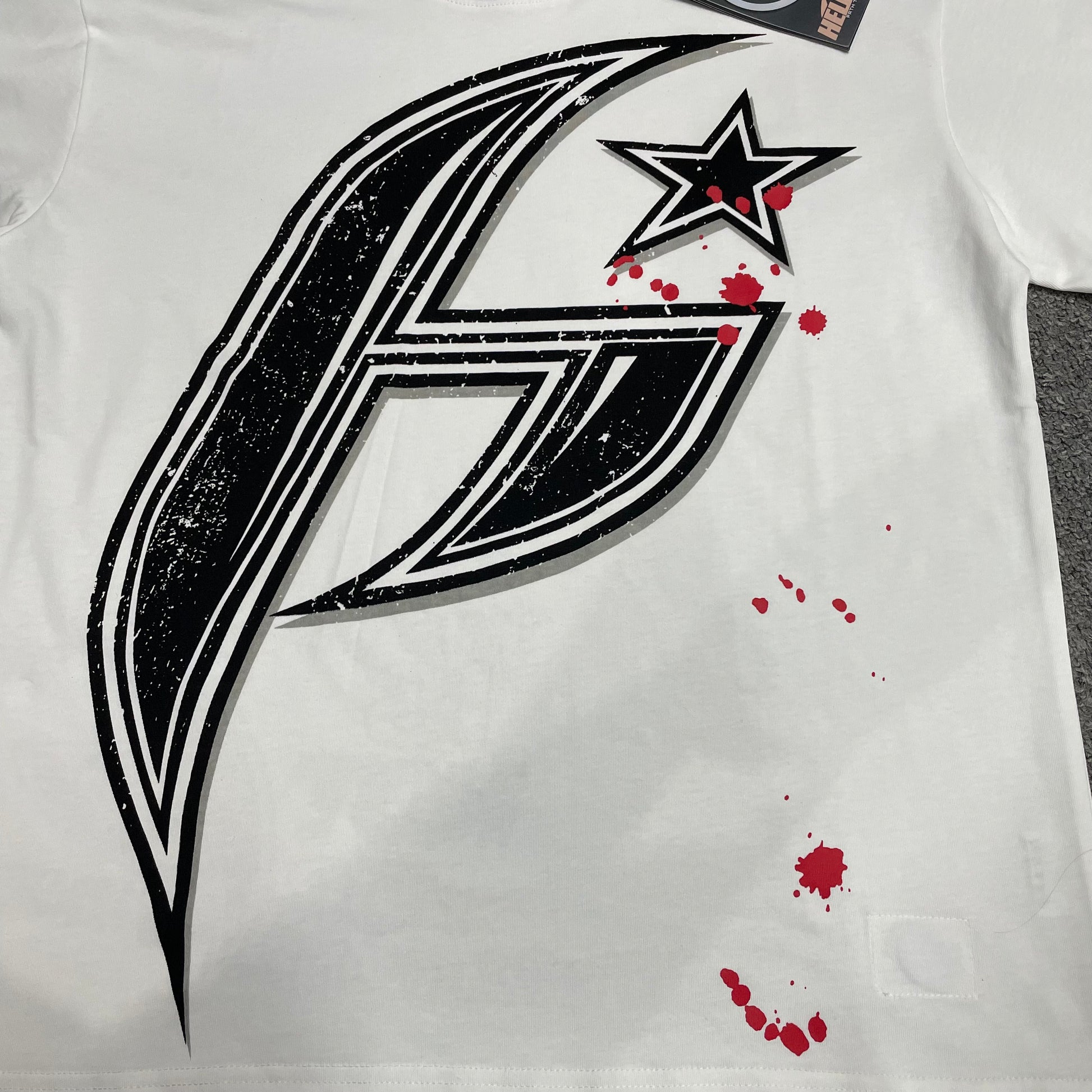 Full oversized black H Star graphic on Hellstar white T-shirt
Close-up of the oversized H Star print on Hellstar white T-shirt
Detailed black distressed graphic and red splatter print on Hellstar H Star Tee
Close-up of the screen-print texture on Hellstar H Star graphic T-shirt
Large black H logo graphic detail on Hellstar white T-shirt