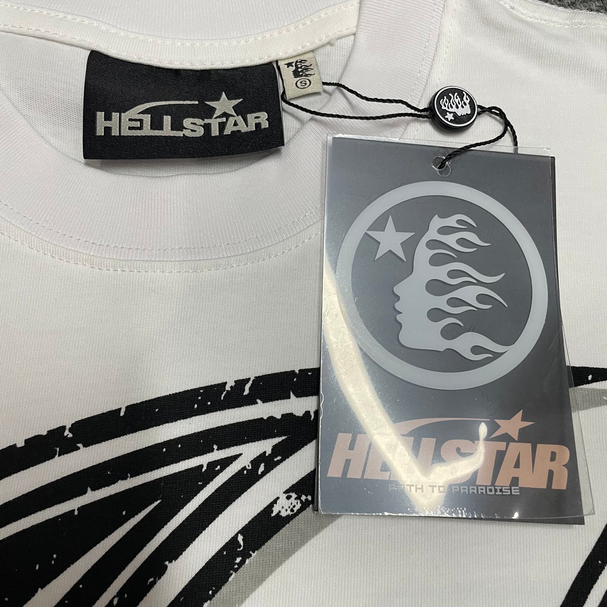Crew neck collar and stitching detail on Hellstar H Star T-shirt
Hellstar woven neck label inside H Star white graphic T-shirt
Hellstar size label detail inside H Star white T-shirt
Hellstar flame logo hangtag front detail on H Star T-shirt