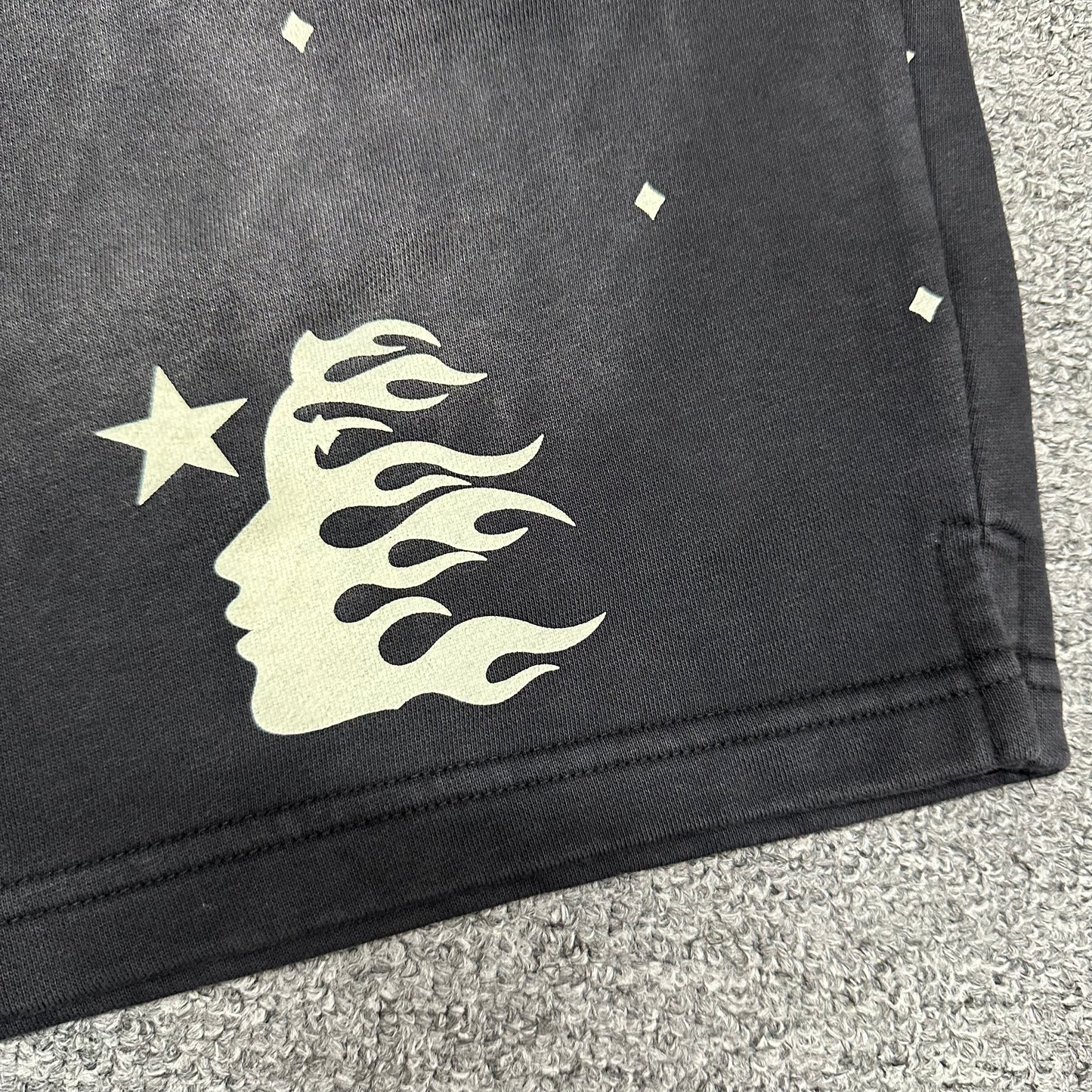 Close-up of Path to Paradise text beneath the Hellstar leg logo
Signature Hellstar flame-face logo printed on the right leg of black shorts
All-over white mini diamond pattern on Hellstar washed black shorts
Close-up of small white diamond graphics on Hellstar black shorts
