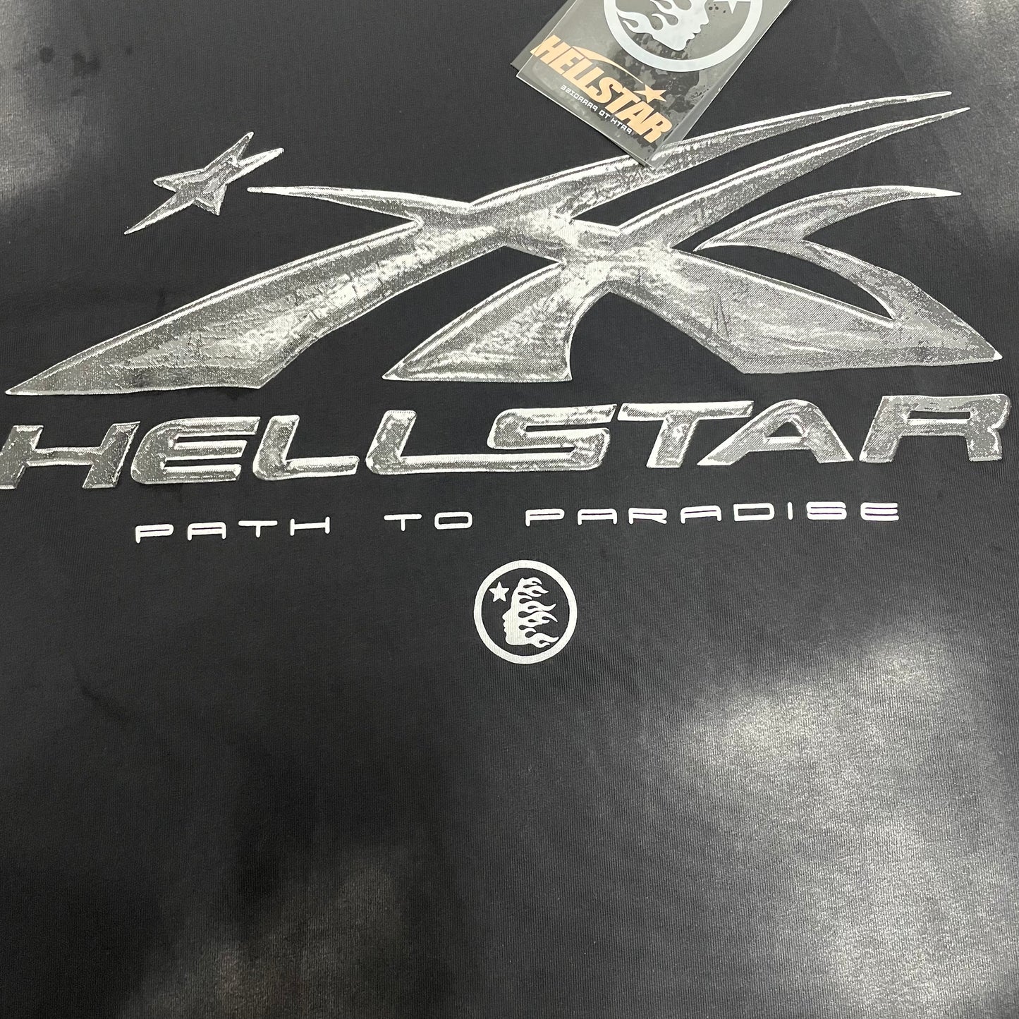 Full metallic silver Hellstar logo graphic on washed black T-shirt
Detailed metallic silver graphic print on Hellstar Chrome Logo T-shirt
Close-up of the metallic silver Hellstar logo surface
Metallic chrome-effect print texture on Hellstar black graphic T-shirt
Path to Paradise lettering detail below the Hellstar chrome logo
Hellstar shooting-star logo detail on Chrome Logo black T-shirt
Distressed black and grey wash effect across Hellstar Chrome Logo T-shirt