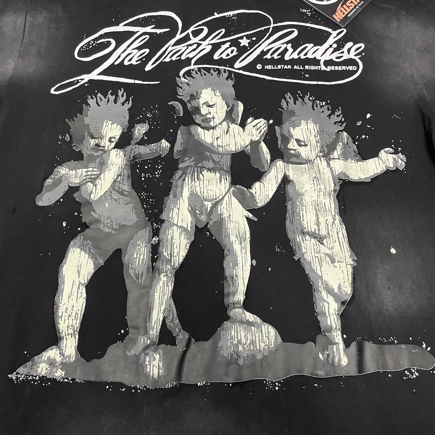 Full three-cherub Path to Paradise graphic on Hellstar washed black T-shirt
Detailed grey white and black cherub artwork on Hellstar graphic T-shirt
Three distressed cherub figures on Hellstar Path to Paradise T-shirt
Close-up of the distressed cherub faces on Hellstar graphic T-shirt
The Path to Paradise script lettering across Hellstar washed black T-shirt