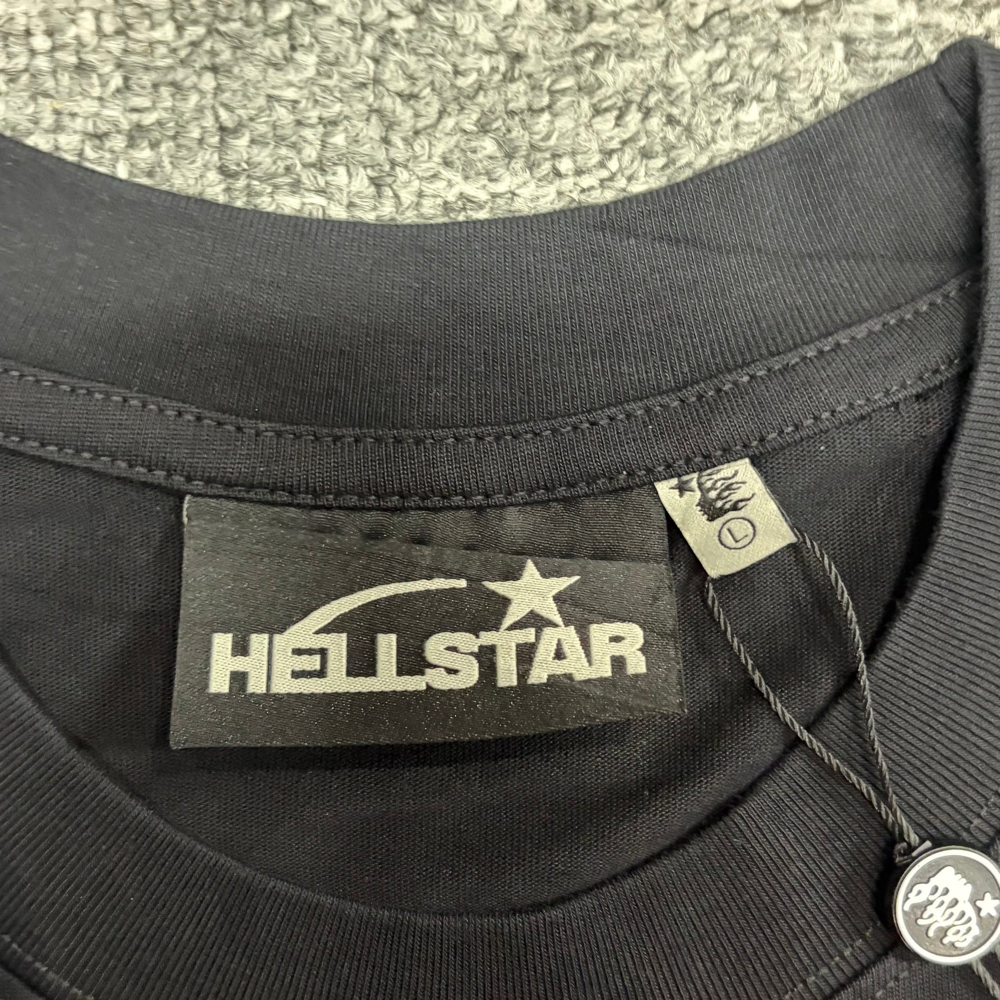 Close-up of ribbed crew neck and neckline of ribbed crew neck and neckline stitching on Hellstar T-shirt
Hellstar neck label inside Studios Cartoon Glitter Logo T-shirt
Size label inside Hellstar Studios washed black T-shirt
Hellstar branded hang tag attached to washed black graphic T-shirt