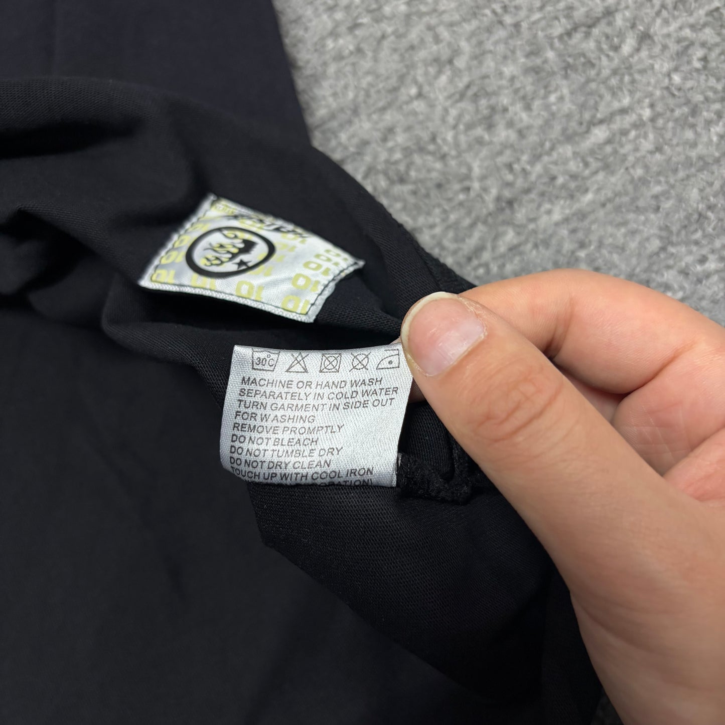 Close-up of hem stitching on Hellstar Studios washed black T-shirt
Fabric composition and care label inside Hellstar Studios T-shirt
NFC tag detail on Hellstar Studios Cartoon Glitter Logo T-shirt