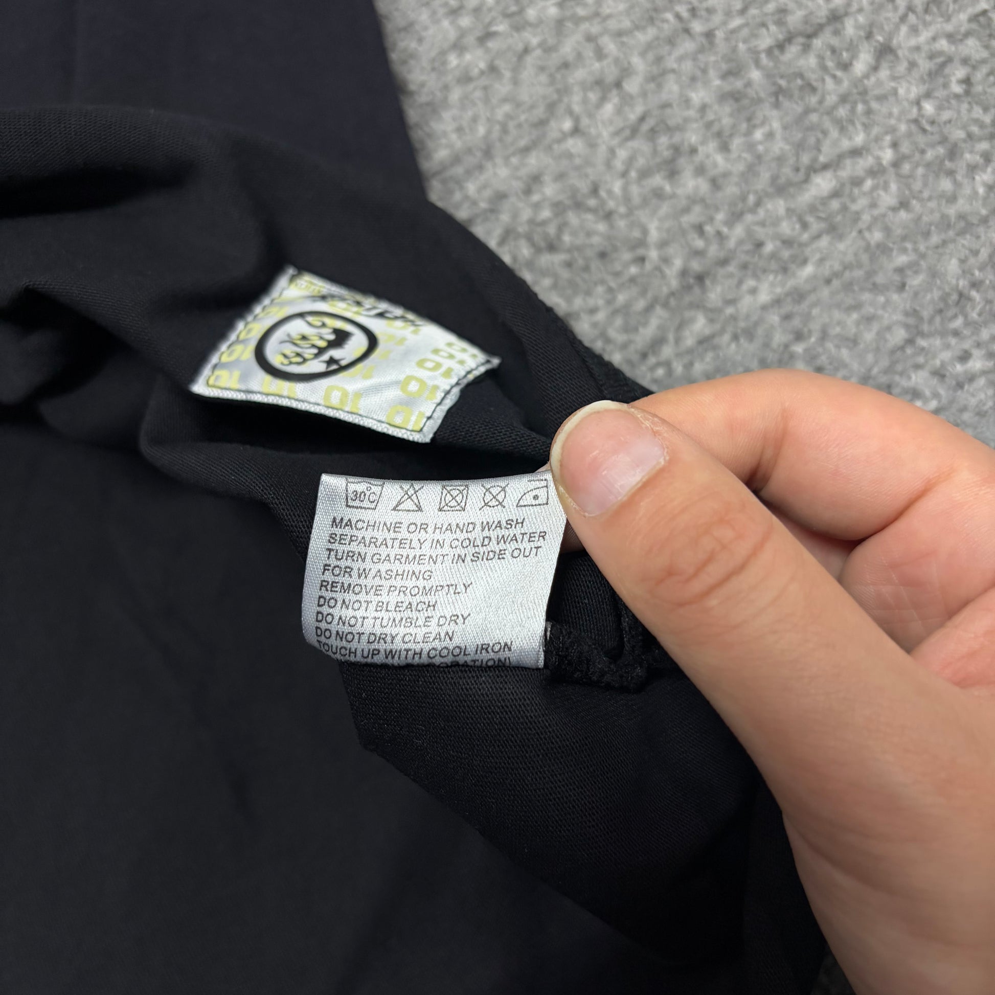 Close-up of hem stitching on Hellstar Studios washed black T-shirt
Fabric composition and care label inside Hellstar Studios T-shirt
NFC tag detail on Hellstar Studios Cartoon Glitter Logo T-shirt