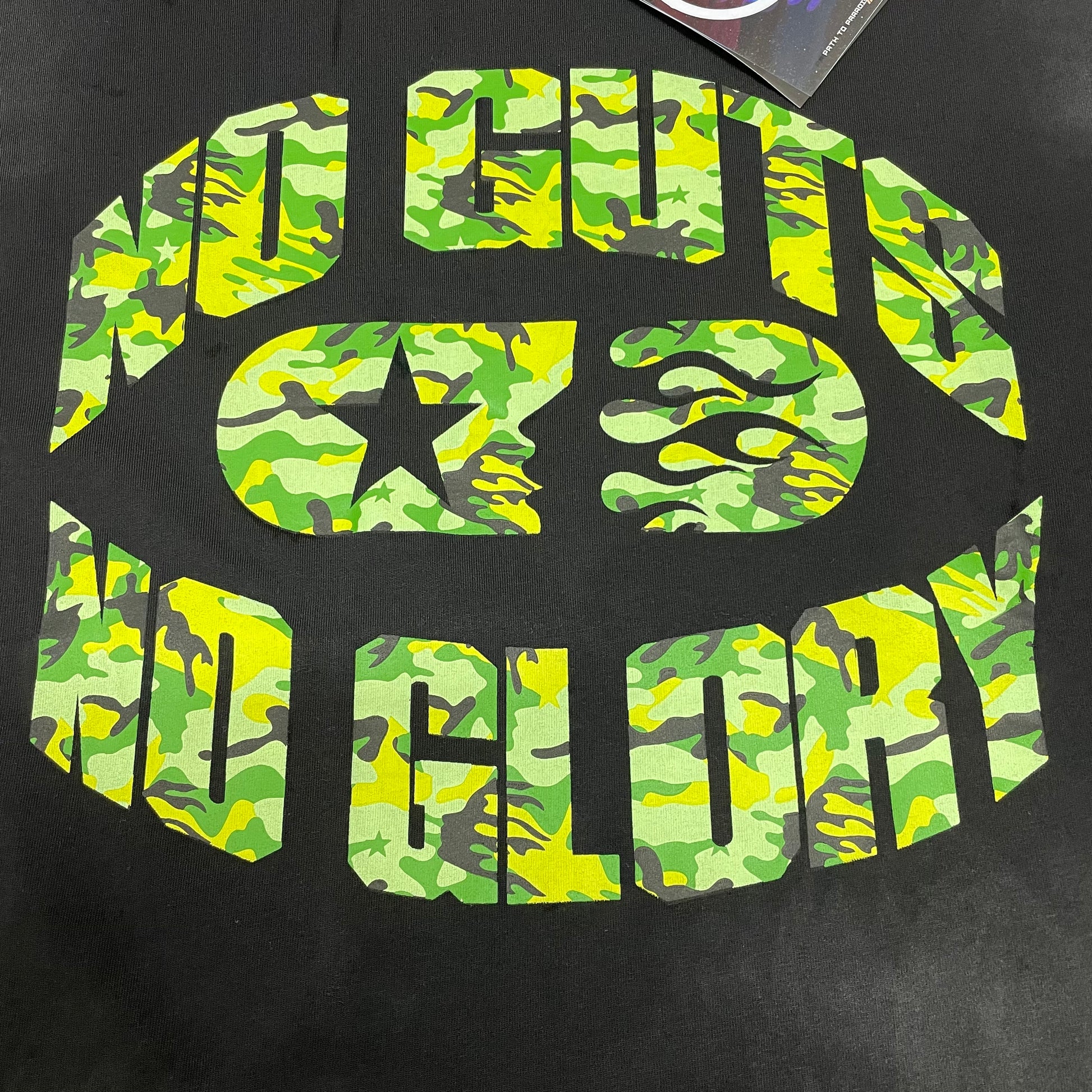 Oversized green camo No Guts No Glory graphic on Hellstar black T-shirt
Hellstar No Guts No Glory circular logo with green camouflage pattern
Close-up of green camo No Guts No Glory graphic print
Detailed view of Hellstar flame face and camouflage print texture
