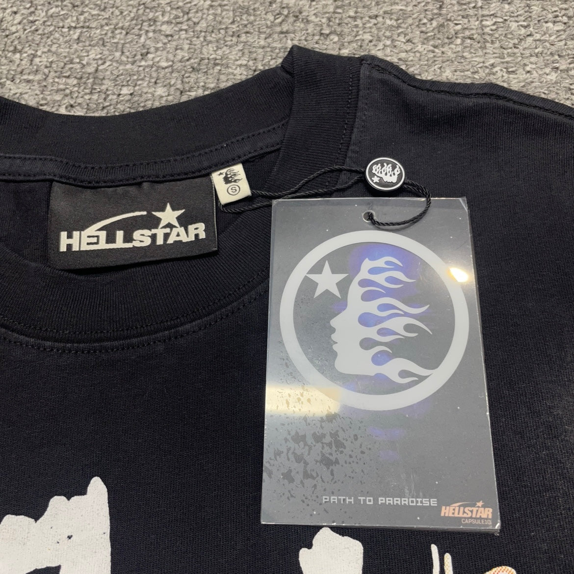 Close-up of ribbed crew neck and reinforced neckline stitching on Hellstar Glory T-shirt
Hellstar branded neck label inside Glory Doll graphic T-shirt
Size label inside Hellstar Glory Doll washed black T-shirt
Hellstar branded hang tag attached to Glory Doll graphic T-shirt