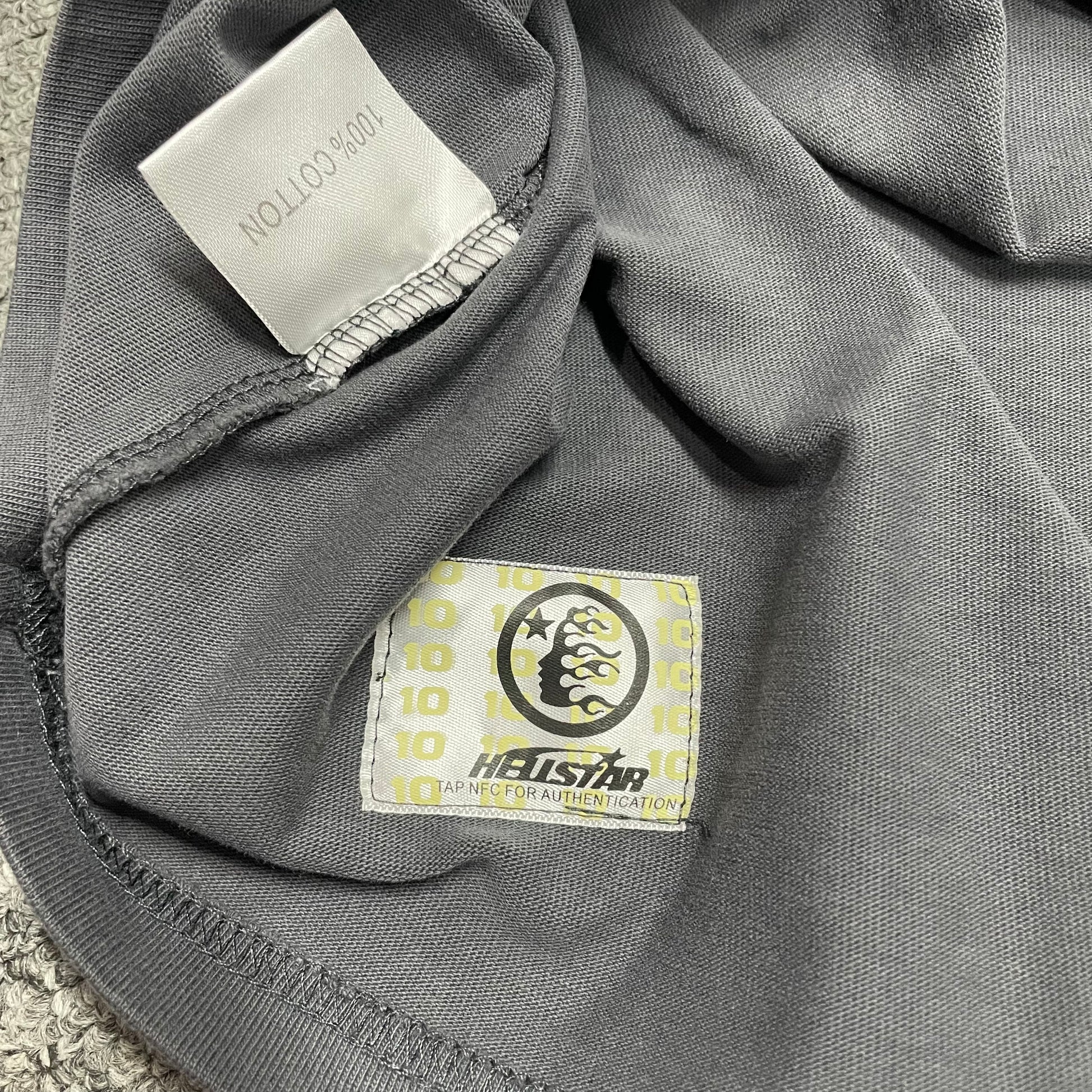 Close-up of bottom hem stitching on Hellstar washed grey T-shirt
Fabric composition and care label inside Hellstar Spray Paint Logo T-shirt
NFC tag detail on Hellstar Spray Paint Logo washed grey T-shirt