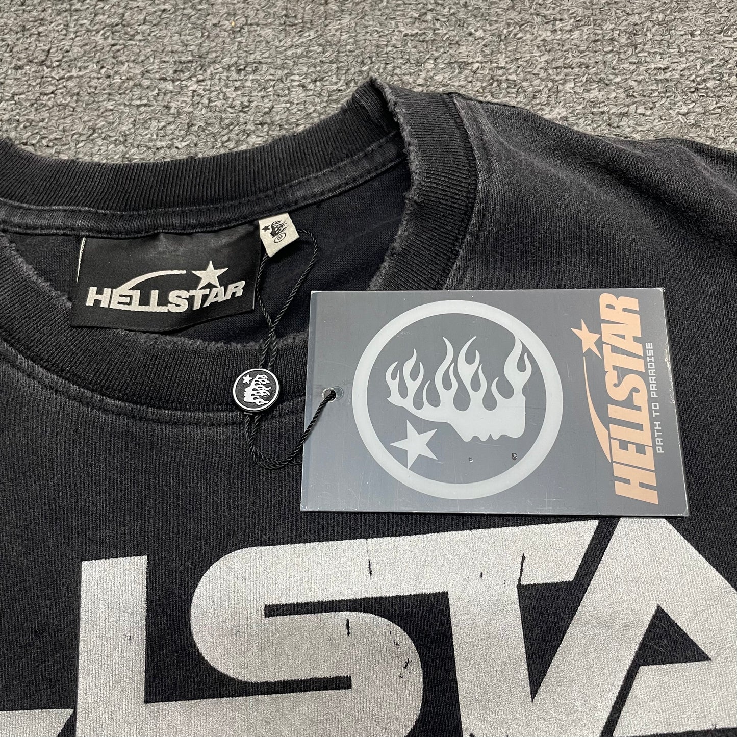 Close-up of distressed ribbed crew neck and neckline stitching on Hellstar Sports T-shirt
Raw-edge distressed collar detail on Hellstar Sports washed black T-shirt
Hellstar branded neck label inside Sports mouth graphic T-shirt
Size label inside Hellstar Sports washed black graphic T-shirt
Hellstar branded hang tag attached to Sports mouth graphic T-shirt
Close-up of Hellstar flame-face hang tag and attachment detail