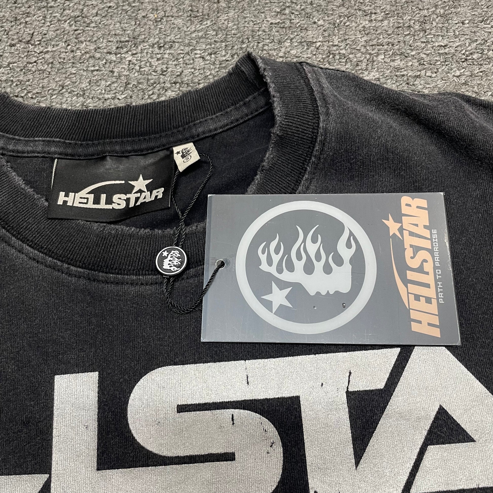 Close-up of distressed ribbed crew neck and neckline stitching on Hellstar Sports T-shirt
Raw-edge distressed collar detail on Hellstar Sports washed black T-shirt
Hellstar branded neck label inside Sports mouth graphic T-shirt
Size label inside Hellstar Sports washed black graphic T-shirt
Hellstar branded hang tag attached to Sports mouth graphic T-shirt
Close-up of Hellstar flame-face hang tag and attachment detail