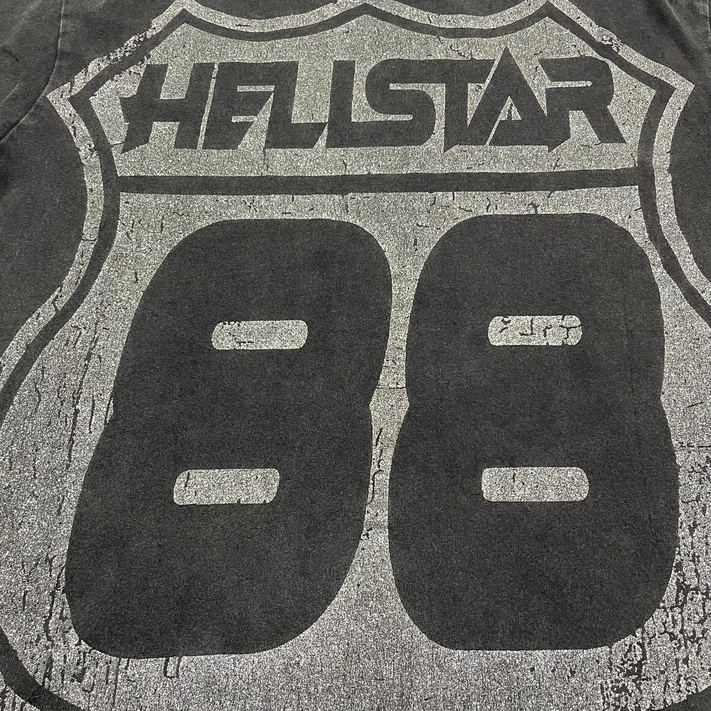 Oversized Hellstar Sports logo and mouth graphic on washed black T-shirt
Distressed Hellstar Sports lettering above a large face and mouth graphic
Close-up of white Hellstar Sports logo print on washed black T-shirt
Close-up of oversized face artwork on Hellstar Sports graphic T-shirt
Close-up of large mouth and tongue graphic on Hellstar Sports T-shirt
Detailed view of teeth lips and tongue artwork on Hellstar Sports T-shirt
Close-up of hand and finger details surrounding the mouth graphic
