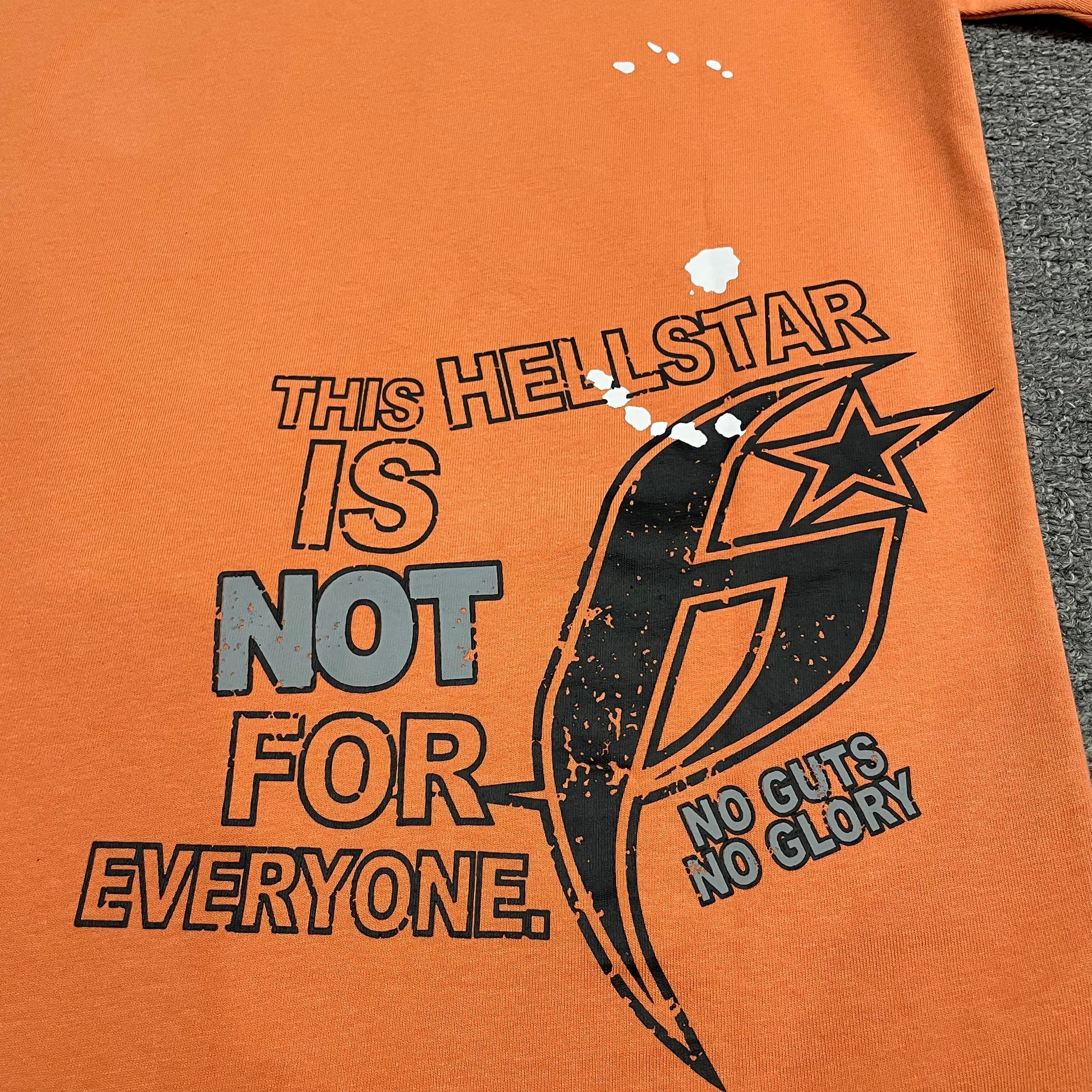 Hellstar statement graphic and H Sharp logo on the back of orange T-shirt
This Hellstar Is Not For Everyone statement with No Guts No Glory graphic
Close-up of Hellstar statement text and H logo back print