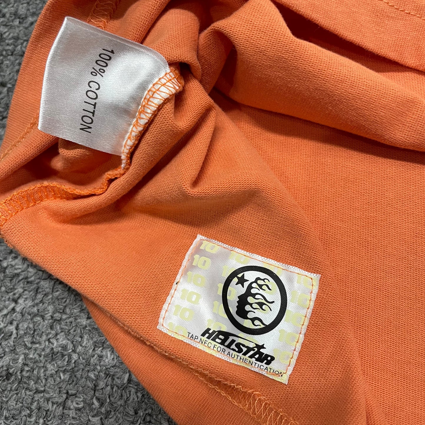 Close-up of bottom hem stitching on Hellstar orange T-shirt
Fabric composition and care label inside Hellstar H Sharp T-shirt
NFC tag detail on Hellstar H Sharp orange graphic T-shirt