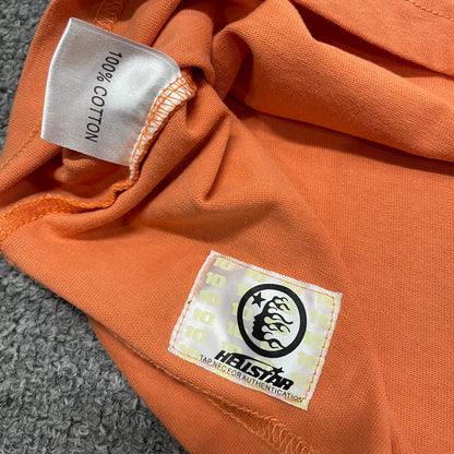 Close-up of bottom hem stitching on Hellstar orange T-shirt
Fabric composition and care label inside Hellstar H Sharp T-shirt
NFC tag detail on Hellstar H Sharp orange graphic T-shirt