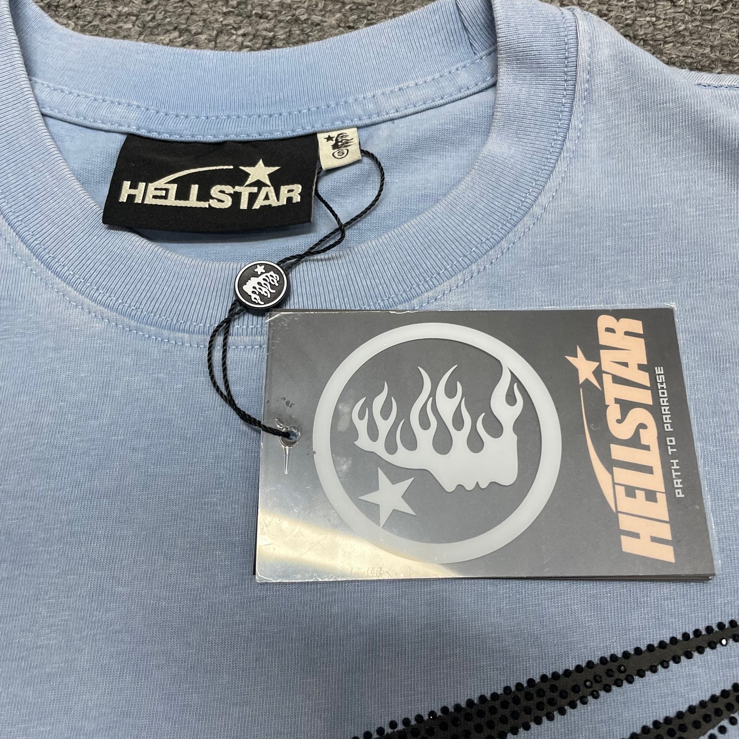 Close-up of ribbed crew neck and neckline stitching on Hellstar T-shirt
Hellstar branded neck label inside Sports Core rhinestone T-shirt
Size label inside Hellstar Sports Core washed blue T-shirt
