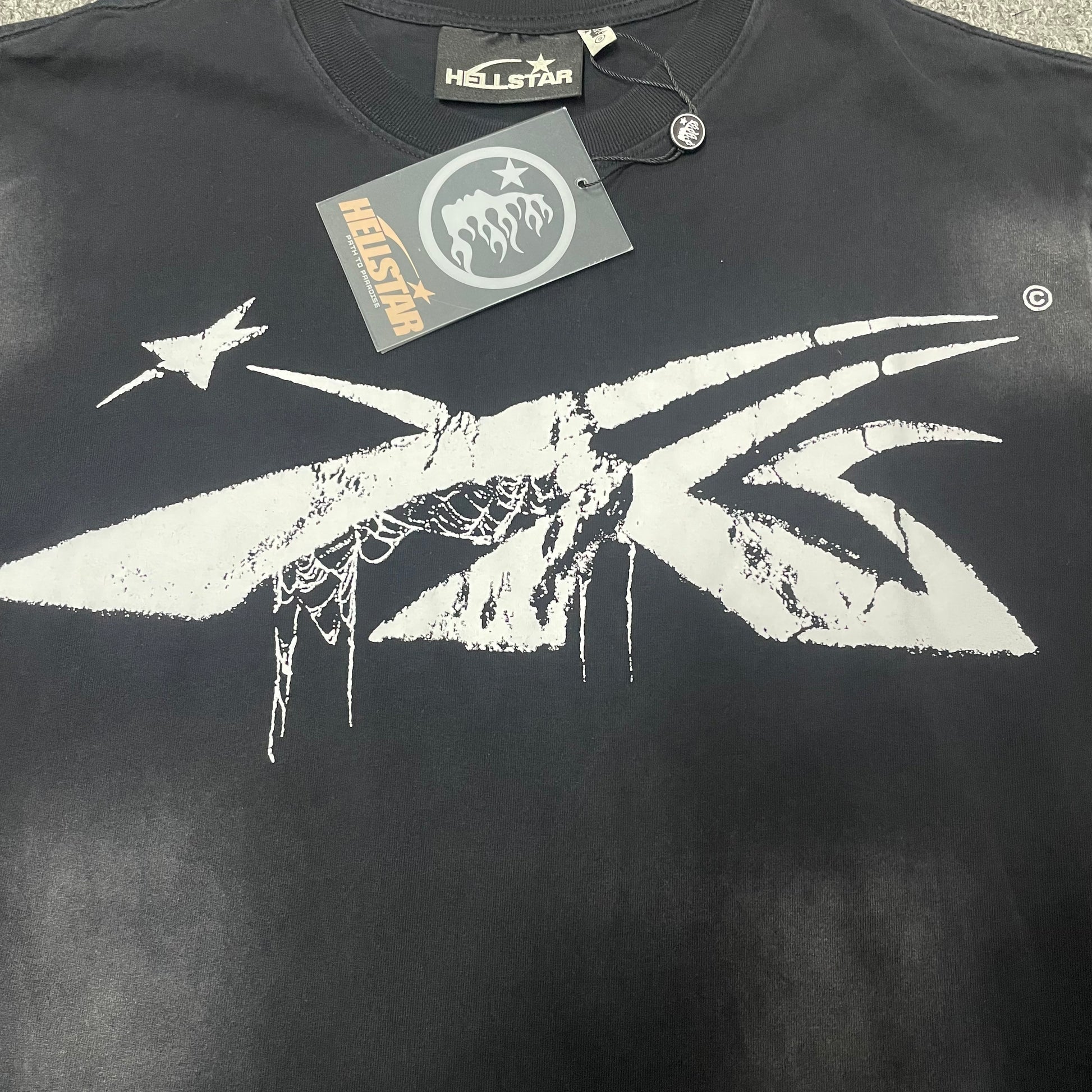 Oversized white Spiderweb Sport logo on Hellstar washed black T-shirt
Distressed athletic-style Hellstar logo with star and hanging spiderweb details
Close-up of white Hellstar Spiderweb Sport logo on black T-shirt
Detailed view of distressed white print texture on Hellstar graphic T-shirt
Close-up of hanging spiderweb details inside the Hellstar Sport logo
Close-up of distressed white star graphic beside the Hellstar Sport logo