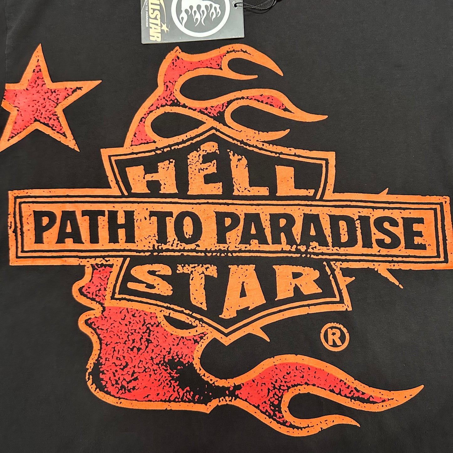 Oversized Hellstar Path To Paradise shield and flame graphic on black T-shirt
Hellstar Path To Paradise shield logo with orange-red flames and star graphic
Close-up of Hellstar Path To Paradise flame graphic on washed black T-shirt
Close-up of distressed Hellstar lettering inside the front shield graphic
Close-up of Path To Paradise text on Hellstar graphic T-shirt
Close-up of orange and red flame details on Hellstar black T-shirt