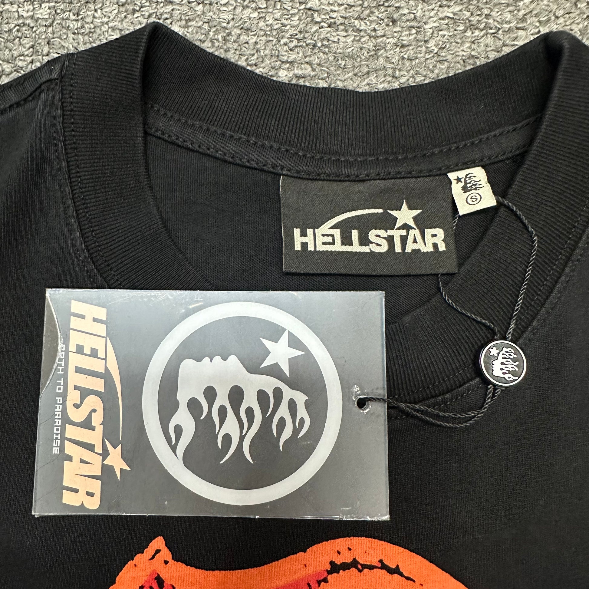 Close-up of ribbed crew neck and neckline stitching on Hellstar T-shirt
Hellstar branded neck label inside Path To Paradise graphic T-shirt
Size label inside Hellstar Path To Paradise washed black T-shirt
Hellstar branded hang tag attached to Path To Paradise graphic T-shirt
Close-up of Hellstar flame-face hang tag and attachment detail