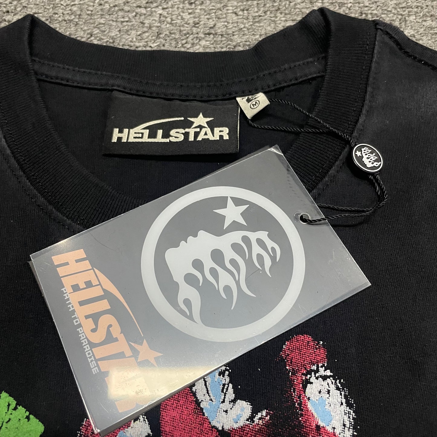 Close-up of ribbed crew neck and neckline stitching on Hellstar sleeveless T-shirt
Close-up of raw-cut armhole finish on Hellstar Worship Hands sleeveless T-shirt
Hellstar branded neck label inside Worship Hands sleeveless T-shirt
Size label inside Hellstar Worship Hands washed black T-shirt
Hellstar branded hang tag attached to Worship Hands sleeveless T-shirt
Close-up of Hellstar flame-face hang tag and attachment detail