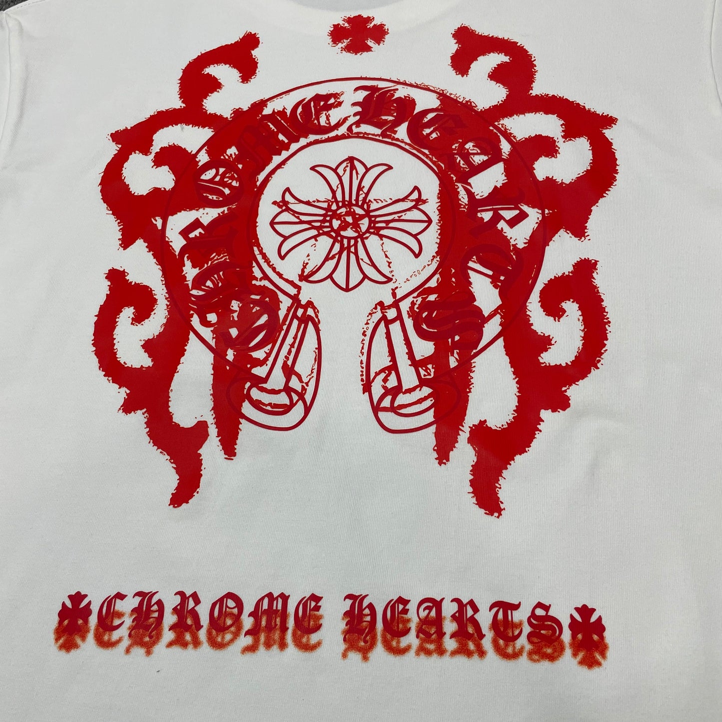 Close-up of oversized red Chrome Hearts floral horseshoe back print on white T-shirt
Detailed Chrome Hearts floral horseshoe and gothic cross graphic printed across the back
Chrome Hearts gothic lettering and lower scroll logo printed on the back of the T-shirt
Chrome Hearts Floral Horseshoe T-shirt oversized back graphic design explanation
The back features an oversized floral horseshoe graphic with gothic lettering, cross details and a lower scroll logo for strong visual impact.