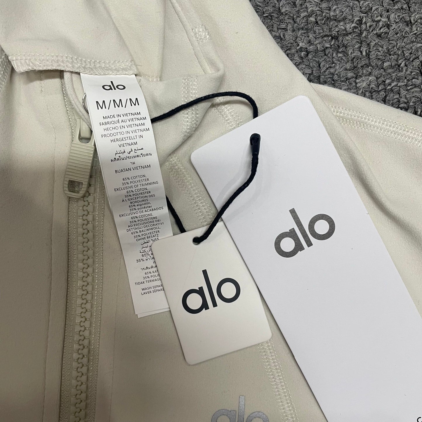 ALO Airbrush Ivory jacket high collar and neckline stitching detail
ALO Airbrush Ivory Corset Jacket neck label and size label close-up
ALO Airbrush Corset Full Zip Jacket in Ivory with branded retail hangtags
ALO Airbrush Ivory jacket care label and fabric information detail
