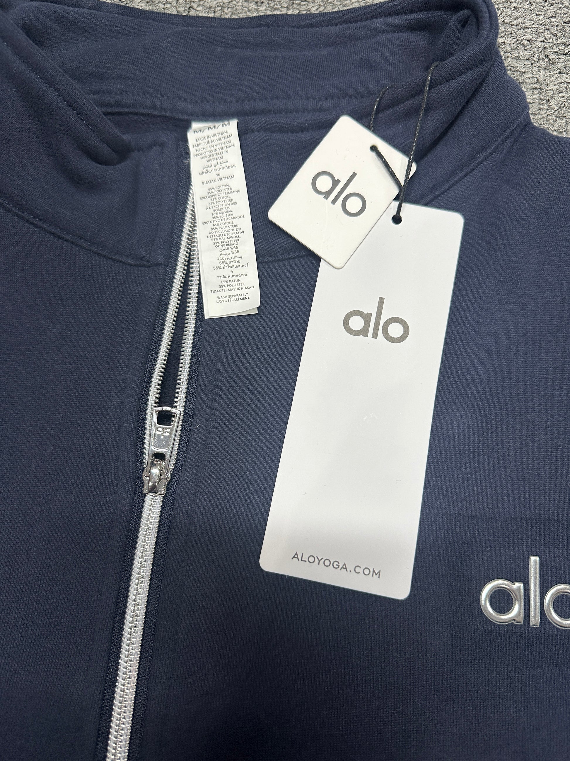 ALO Accolade Navy pullover stand collar and quarter zip construction detail
ALO Accolade Navy quarter zip pullover neck label and size tag detail
ALO Accolade Navy quarter zip pullover with branded retail hangtags
ALO Accolade Navy pullover care label and fabric information detail
