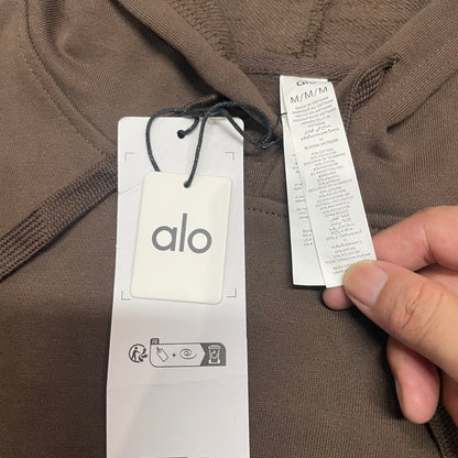 ALO Accolade Espresso hoodie neckline, hood and drawstring construction detail
ALO Accolade Espresso hoodie neck label and size label close-up
ALO Accolade Espresso hoodie with branded retail hangtags
ALO Accolade Espresso hoodie care label and fabric information detail