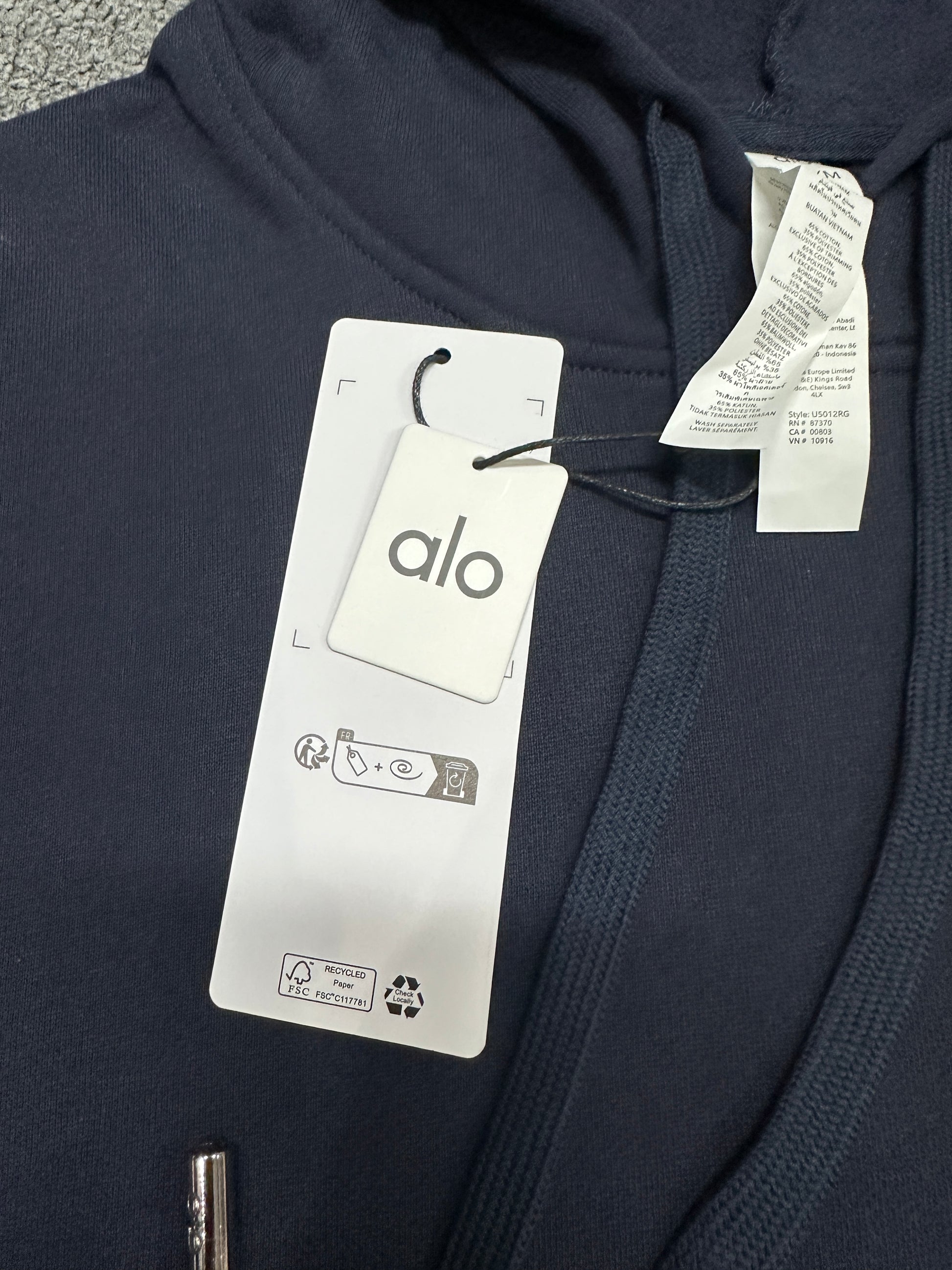 ALO Accolade Navy hoodie neckline, hood and drawstring construction detail
ALO Accolade Navy hoodie neck label and size label close-up
ALO Accolade Navy hoodie with branded retail hangtags
ALO Accolade Navy hoodie care label and fabric information detail