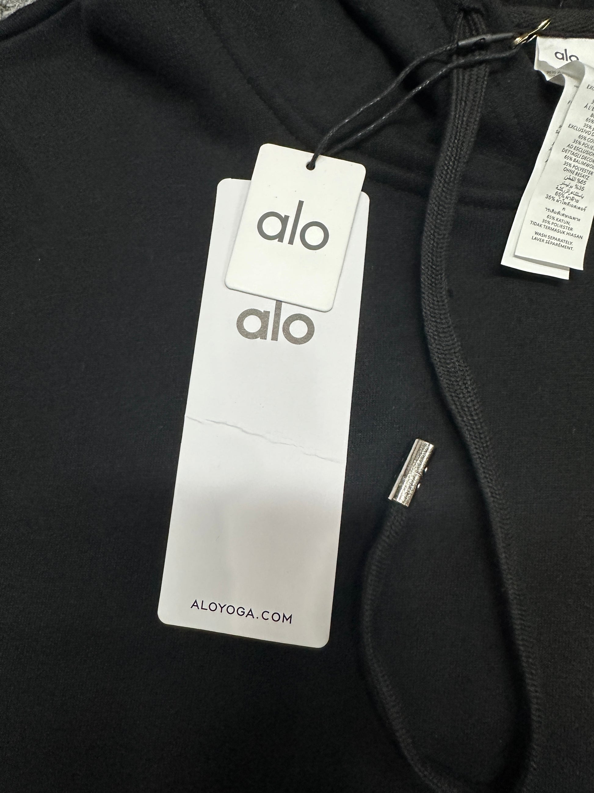 ALO Accolade Black hoodie neck label and size label close-up
ALO Accolade Black hoodie with branded retail hangtags
ALO Accolade Black hoodie care label and fabric information detail