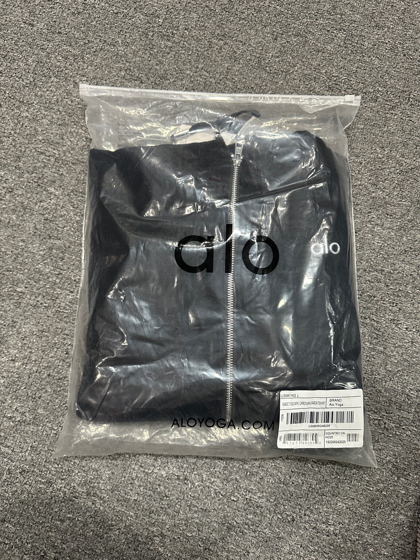 ALO Accolade Black full zip hoodie folded inside branded zip packaging bag