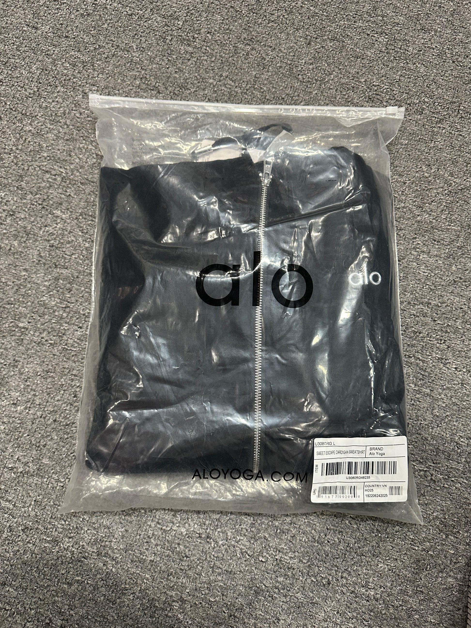 ALO Accolade Black full zip hoodie folded inside branded zip packaging bag