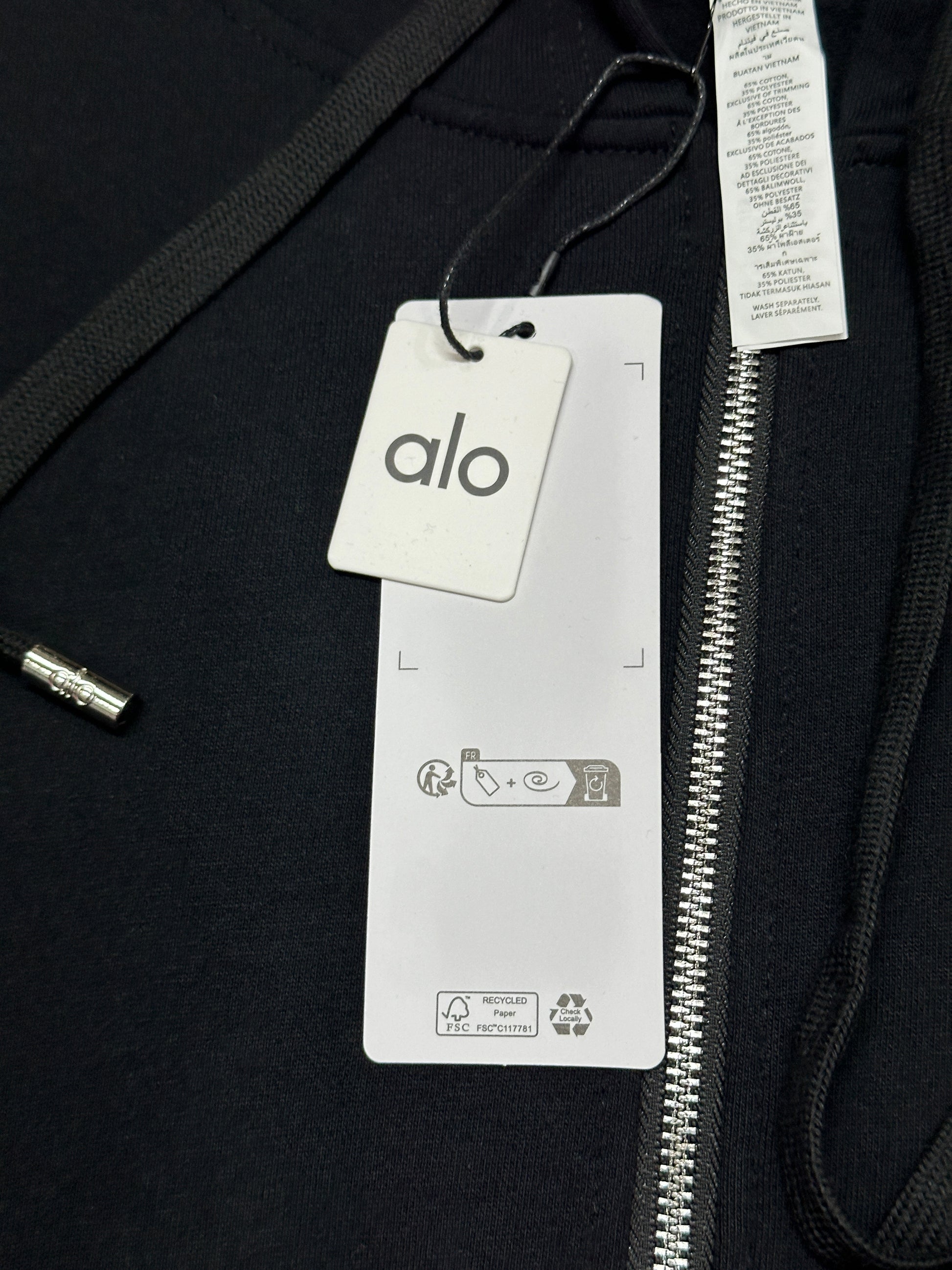 ALO Accolade Black full zip hoodie neckline, hood and drawstring construction detail
ALO Accolade Black full zip hoodie neck label close-up
ALO Accolade Black full zip hoodie size label detail
ALO Accolade Black full zip hoodie with branded retail hangtags