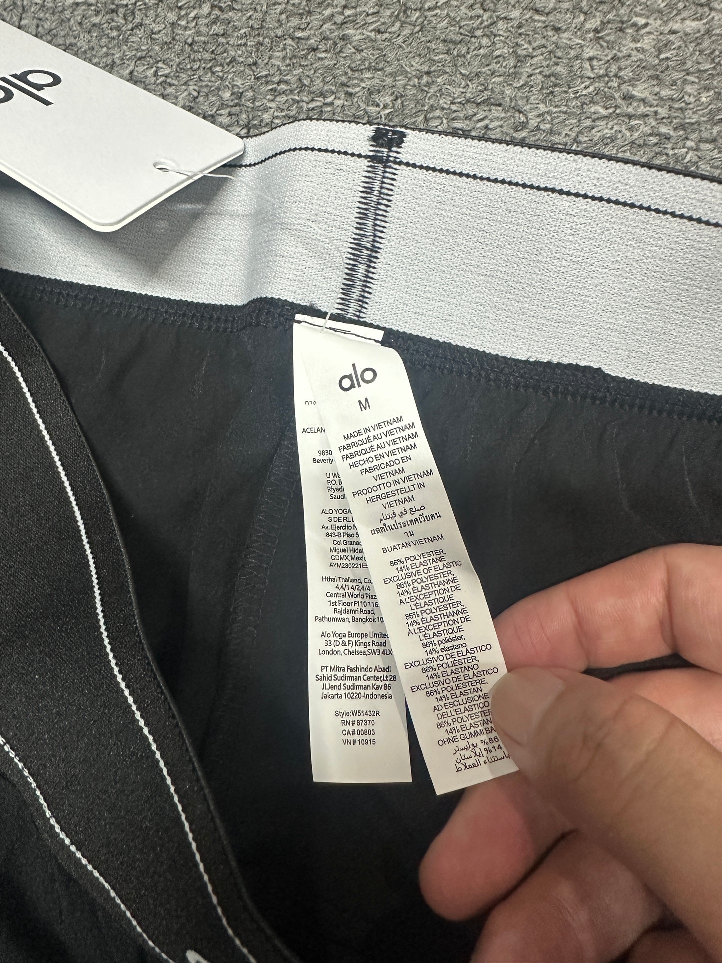 Alo Yoga Pursuit Trouser Elastic Contrast Striped Waistband Stitching Detail
Alo Yoga Pursuit Trouser Inner Woven Waist Tag and Size Label
Alo Yoga Authentic Retail Hangtag with Barcode Tag
Alo Yoga Care Label Polyester Spandex Fabric Washing Instructions
