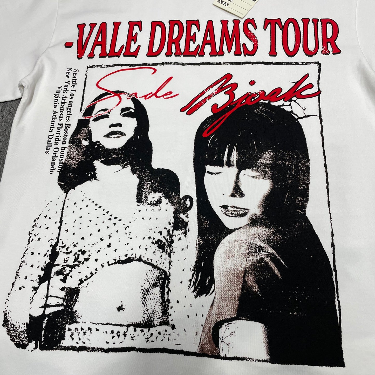 Vale Forever Dreams Tour Tee full Sade and Bjork front graphic
Vale Forever Dreams Tour Tee Sade and Bjork portrait graphic
Sade and Bjork black and white portrait print detail on cream tee
Vale Dreams Tour distressed red lettering print close-up
Sade Bjork red script lettering detail on Vale Forever graphic tee
Vale Forever Dreams Tour Tee distressed vintage front print detail