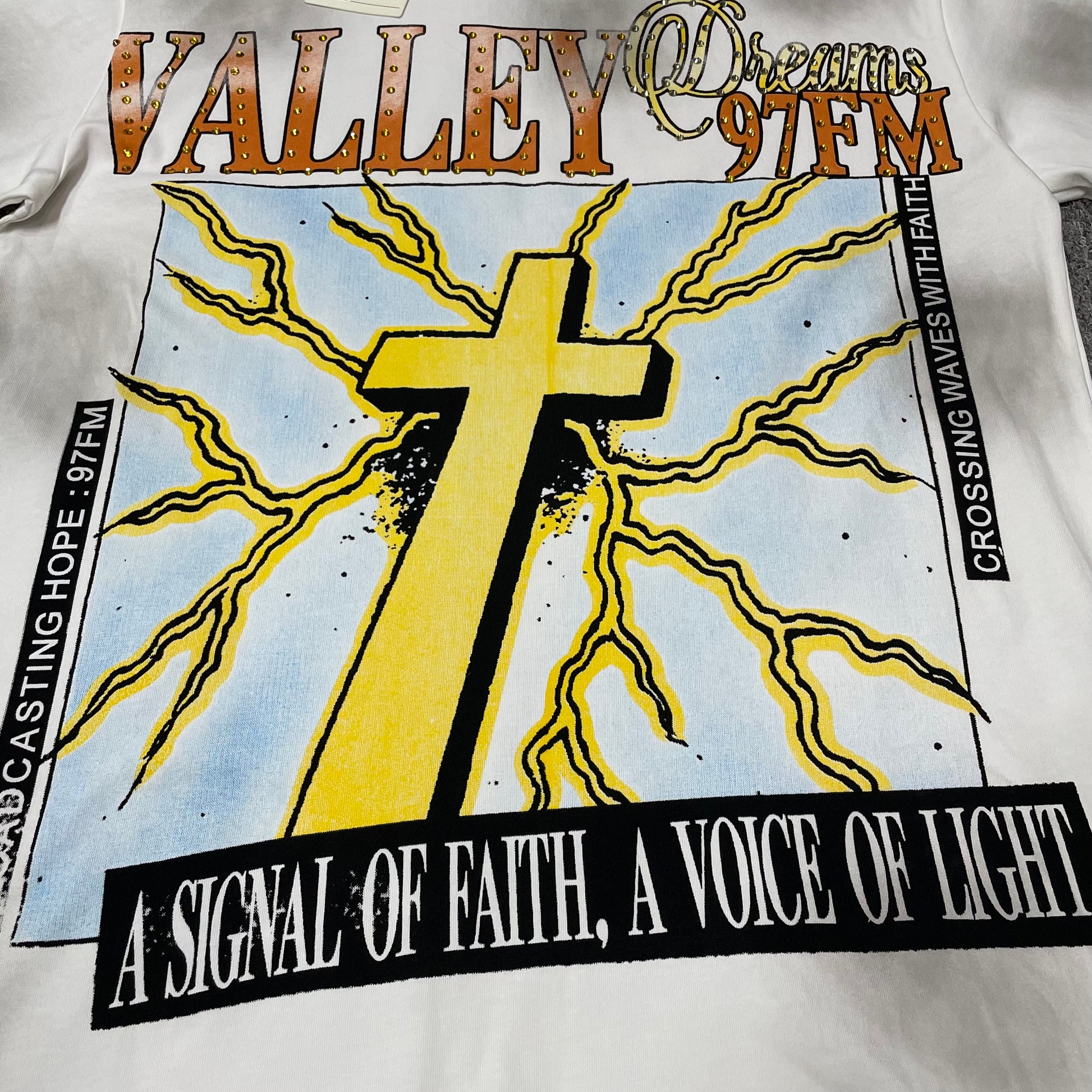 Vale Forever Thunder Cross Bling Tee full cross and lightning front graphic
Vale Forever Thunder Cross Bling Tee oversized yellow cross graphic
Vale Forever Thunder Cross Bling Tee distressed graphic print close-up
Vale Forever Thunder Cross Bling Tee crystal Valley lettering detail
Vale Forever Thunder Cross Bling Tee Dreams 97FM lettering detail
Vale Forever Thunder Cross Bling Tee sparkling crystal embellishment close-up
Vale Forever Thunder Cross Bling Tee yellow cross print detail