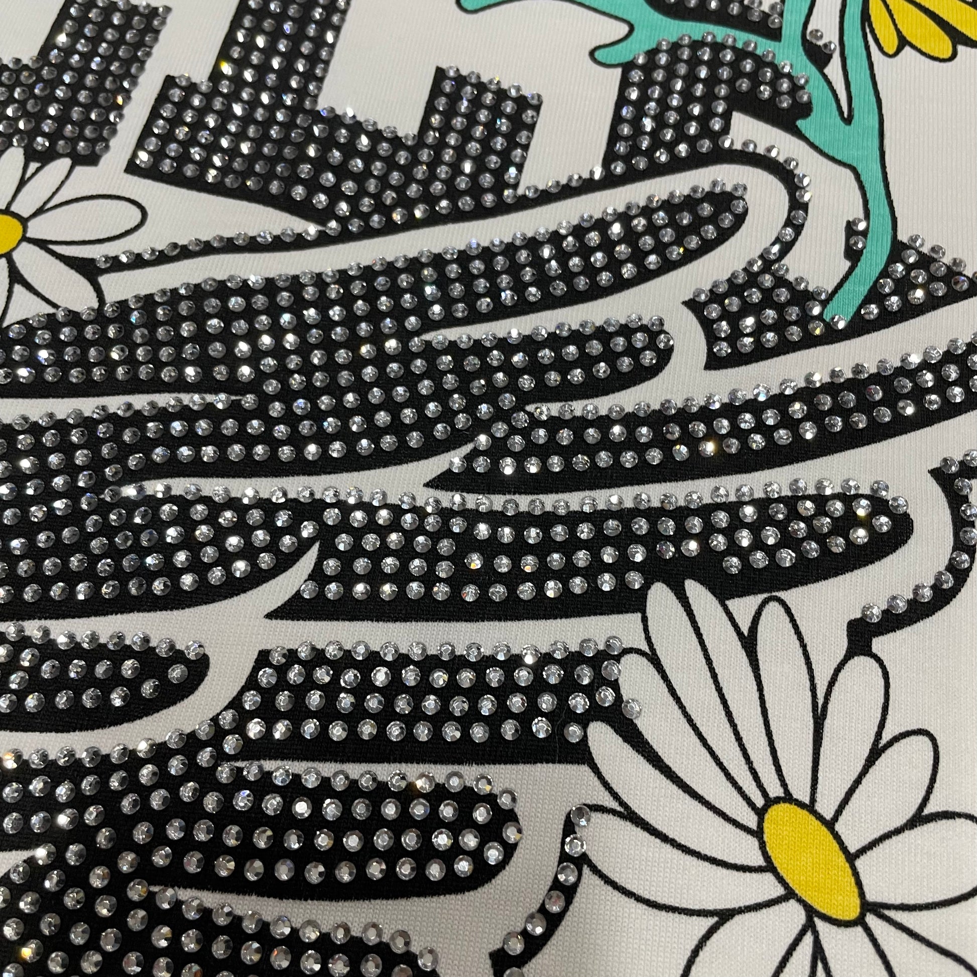 Vale Forever Valley Track Tee full winged shoe and floral front graphic
Vale Forever Valley Track Tee winged track-shoe and floral artwork
Vale Forever Valley Track Tee detailed floral and wing graphic close-up
Vale Forever Valley Track Tee crystal Valley lettering detail
Vale Forever Valley Track Tee crystal Track lettering detail
Vale Forever Valley Track Tee black crystal embellishment close-up
Vale Forever Valley Track Tee winged running shoe graphic detail